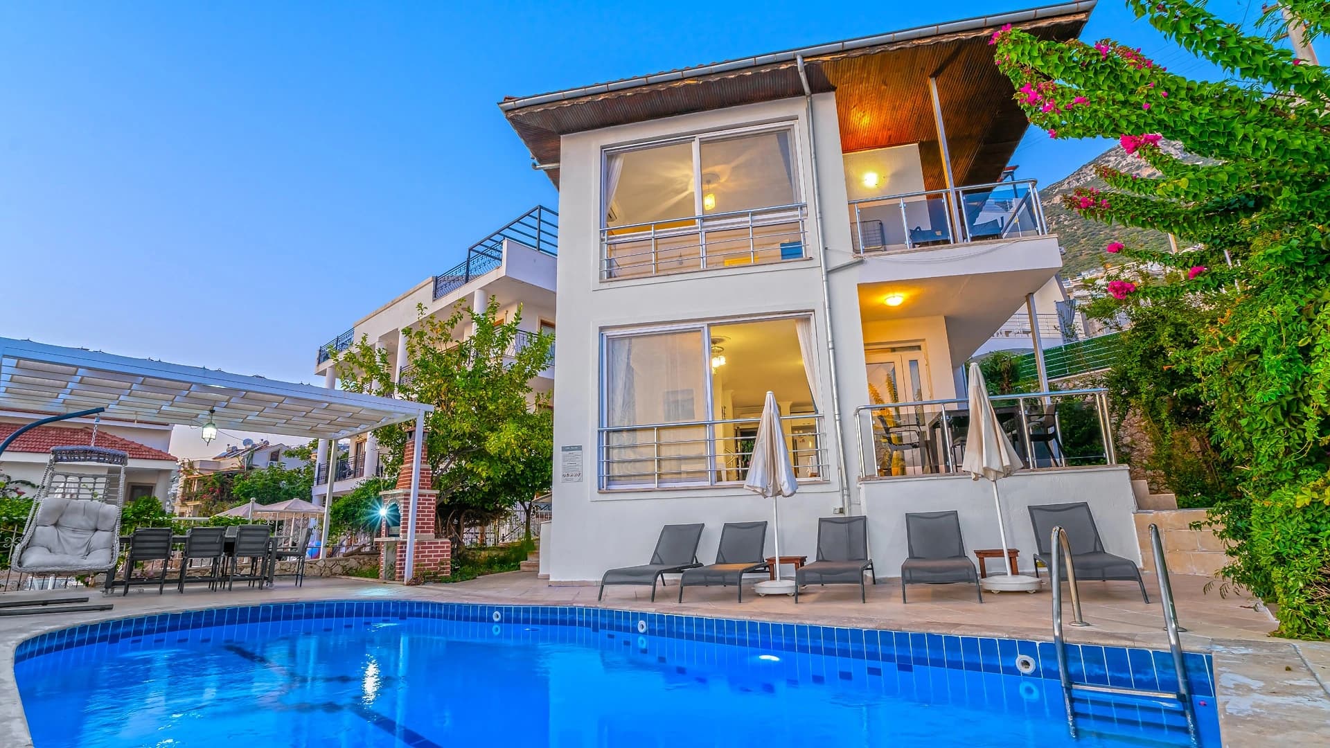 Modern white villa with pristine blue pool and lounge seating, captured during golden hour.