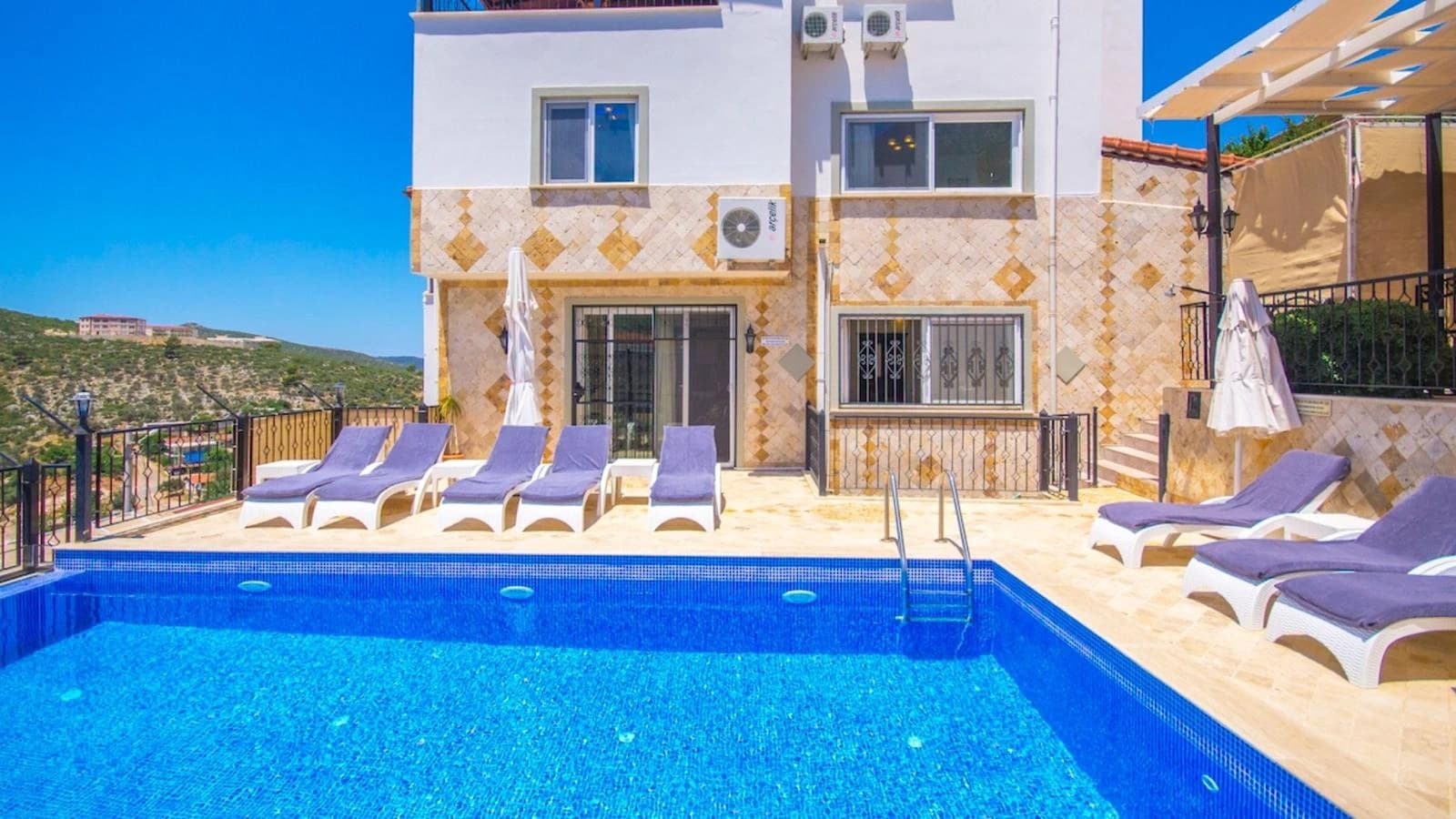 Stunning poolside terrace with crystal-clear water, multiple loungers, and hillside views.