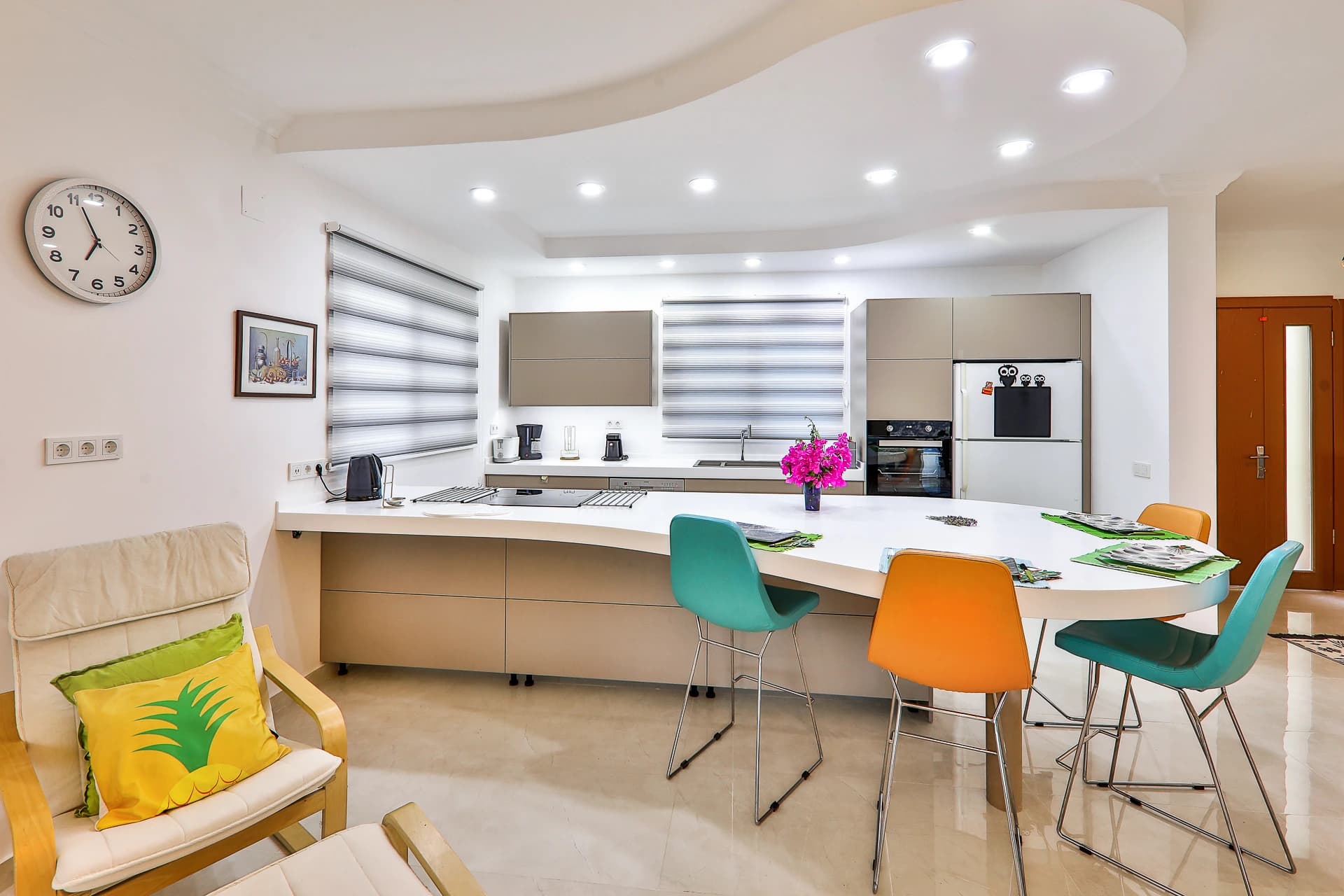 Modern dining area with kitchen, colorful seating, and elegant lighting.