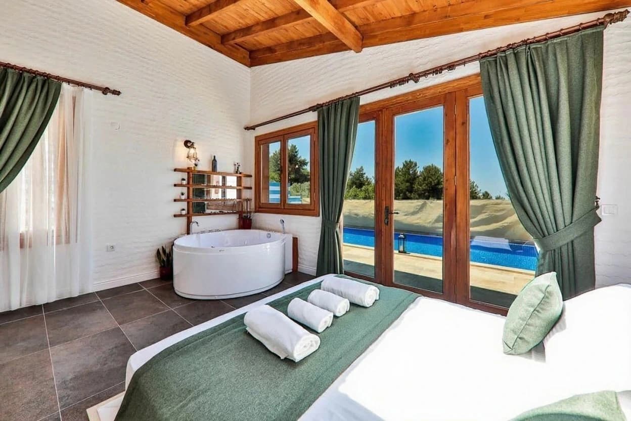 Spacious bedroom suite with king bed, freestanding bathtub, pool view, and glass doors to terrace.