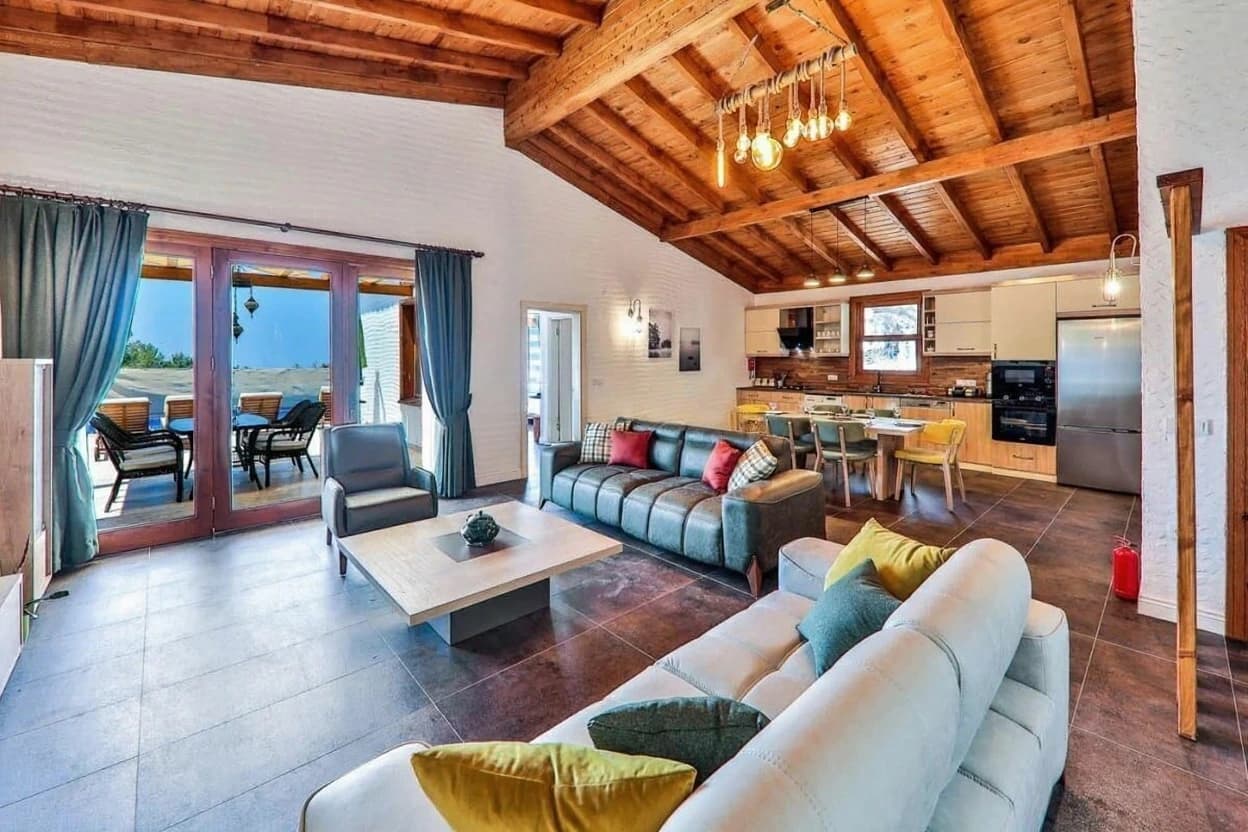 Spacious open-plan living area with exposed wooden beams, modern furnishings, and direct terrace access.