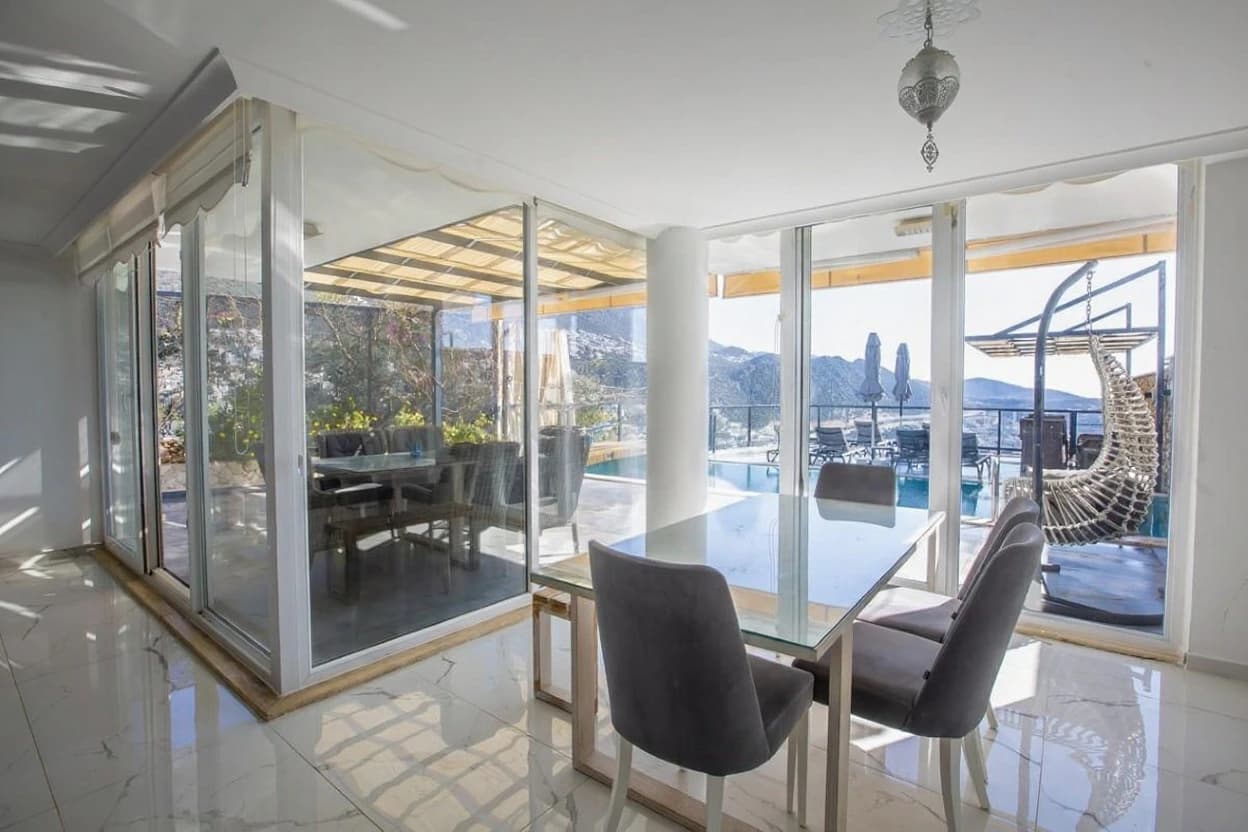 Sophisticated dining space with panoramic mountain and pool views through floor-to-ceiling glass doors.