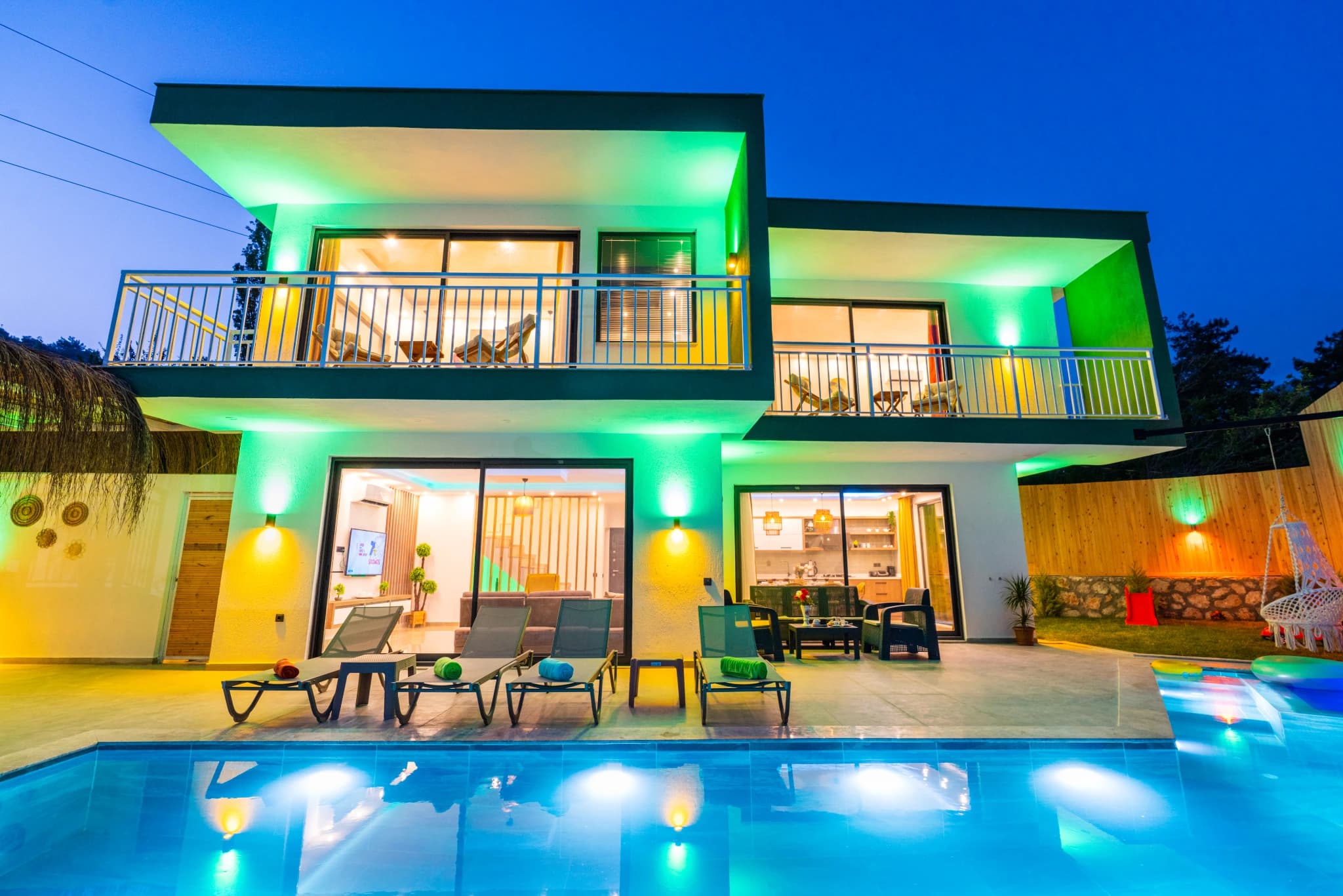 Modern villa exterior with illuminated private pool and multi-level balconies at night.