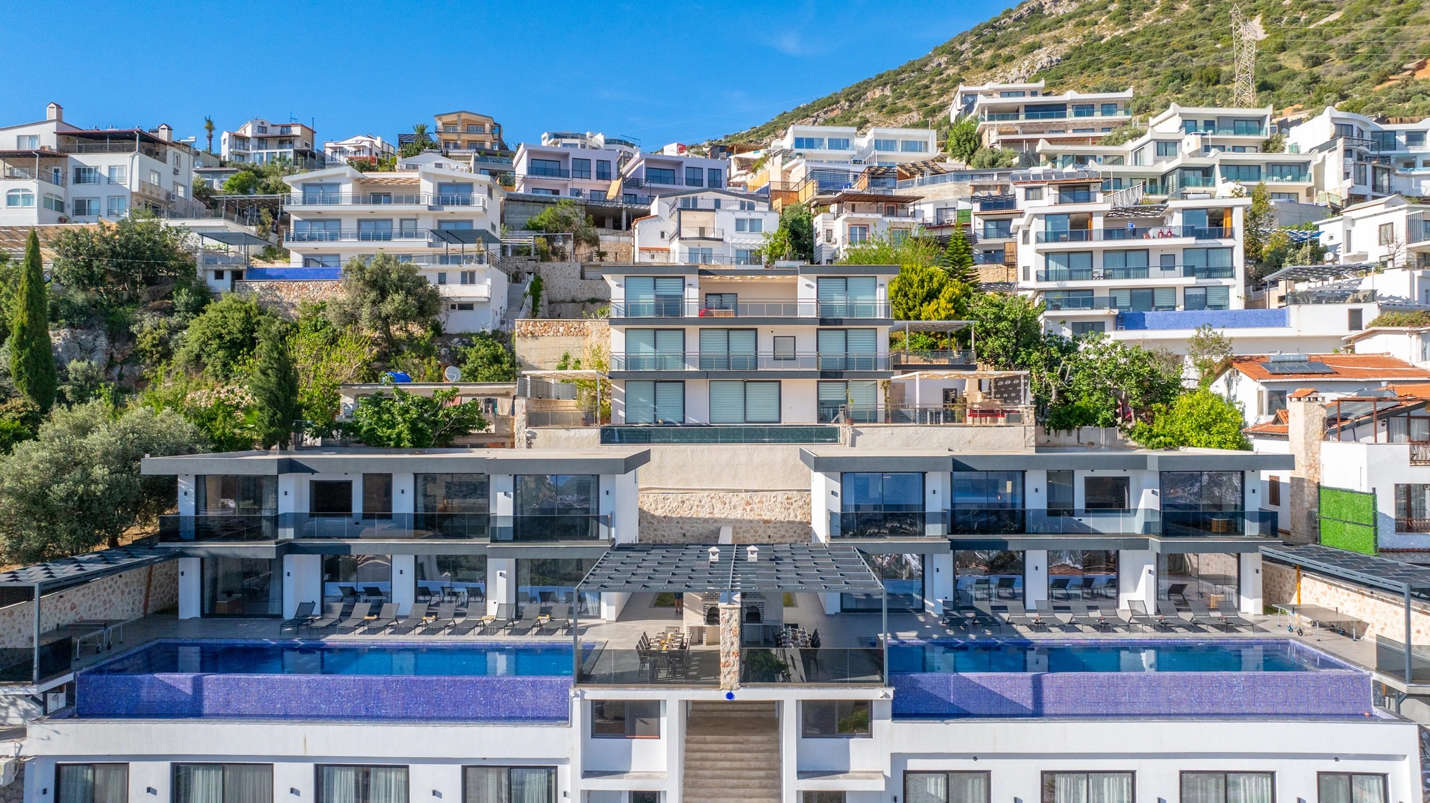 Elevated exterior view showcasing dual pools, hillside setting, and Mediterranean scenery.