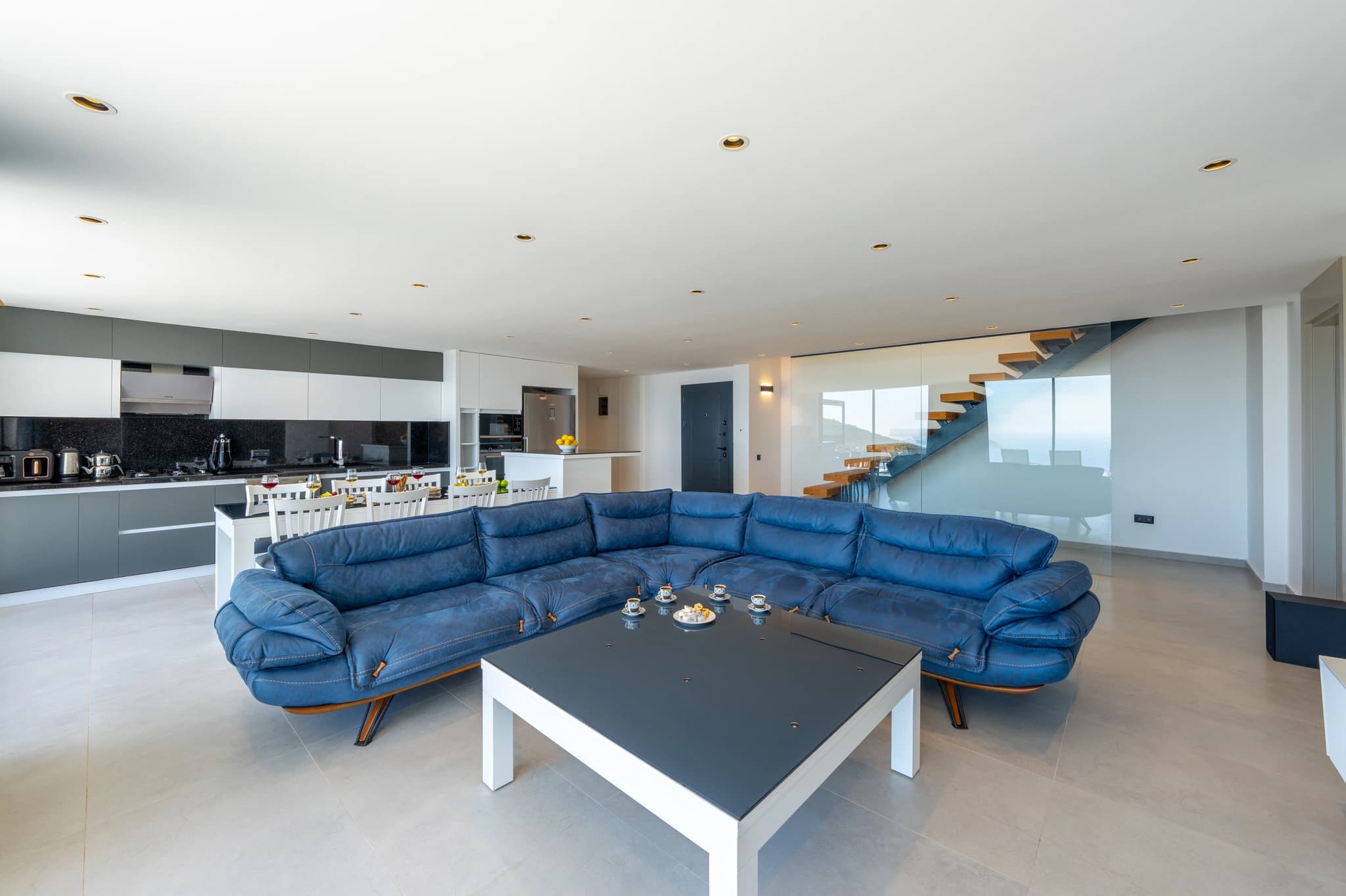Spacious open-plan living room with expansive blue sectional and contemporary furnishings overlooking kitchen and staircase.