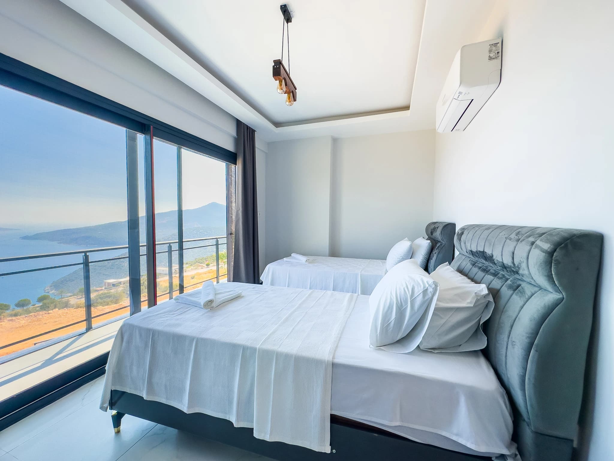 Spacious guest bedroom with two single beds, stunning sea and mountain views from balcony, and ensuite bathroom.