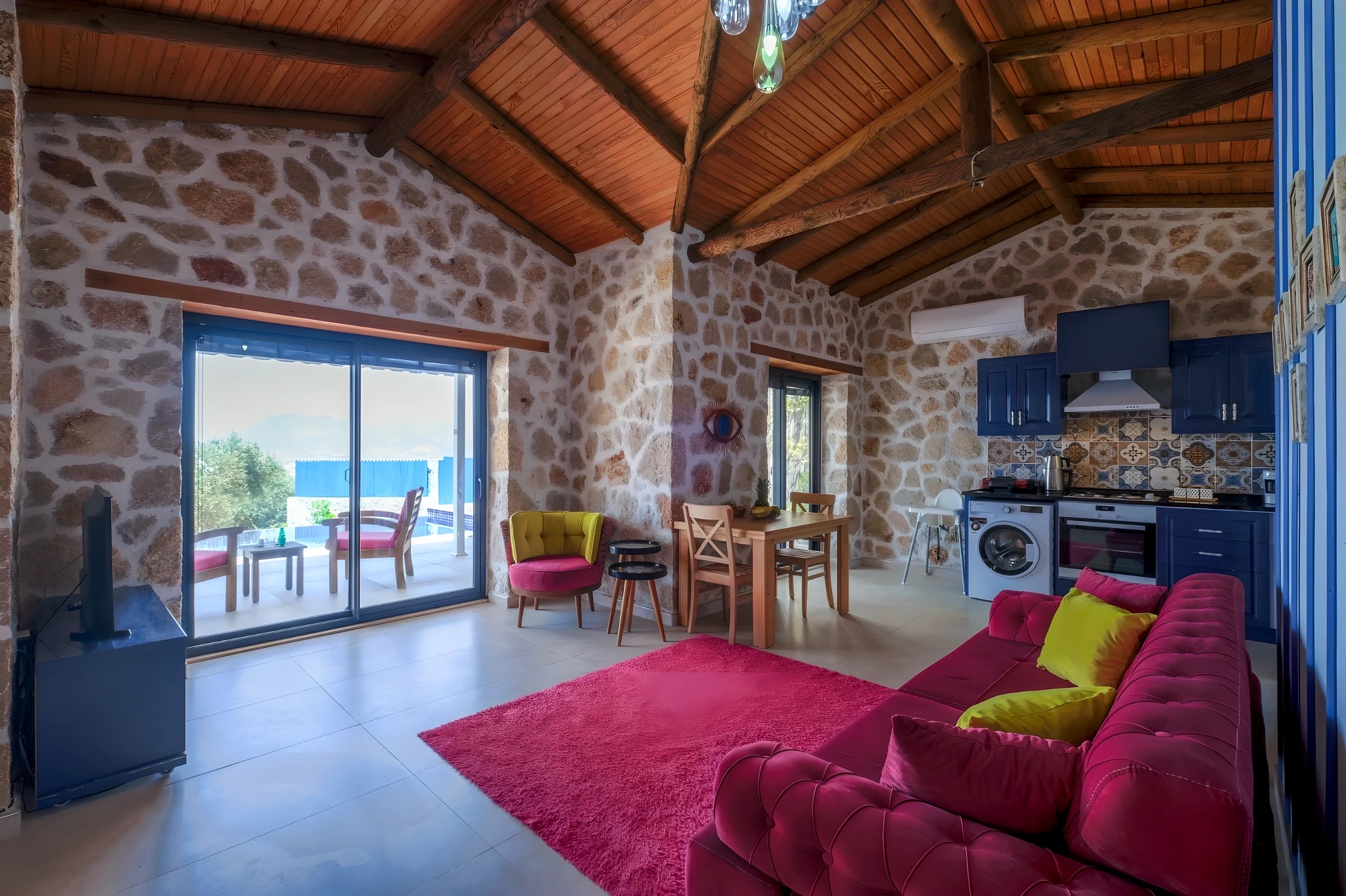 Open-plan living and kitchen space with vibrant magenta sofa and sea view access.