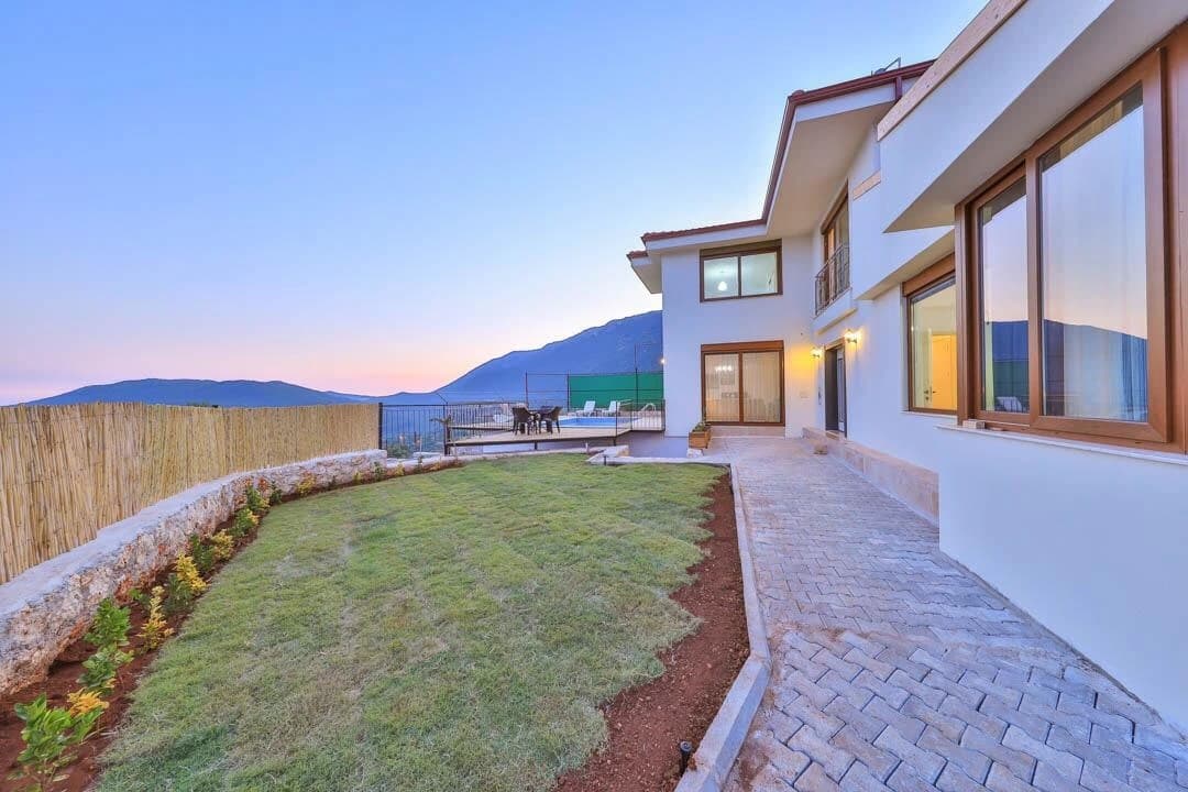 Abgeschiedene 3-Zimmer-Villa mit privatem Pool und Bergblick in Kaş – Modern villa exterior at dusk with terrace, manicured lawn, and mountain views.