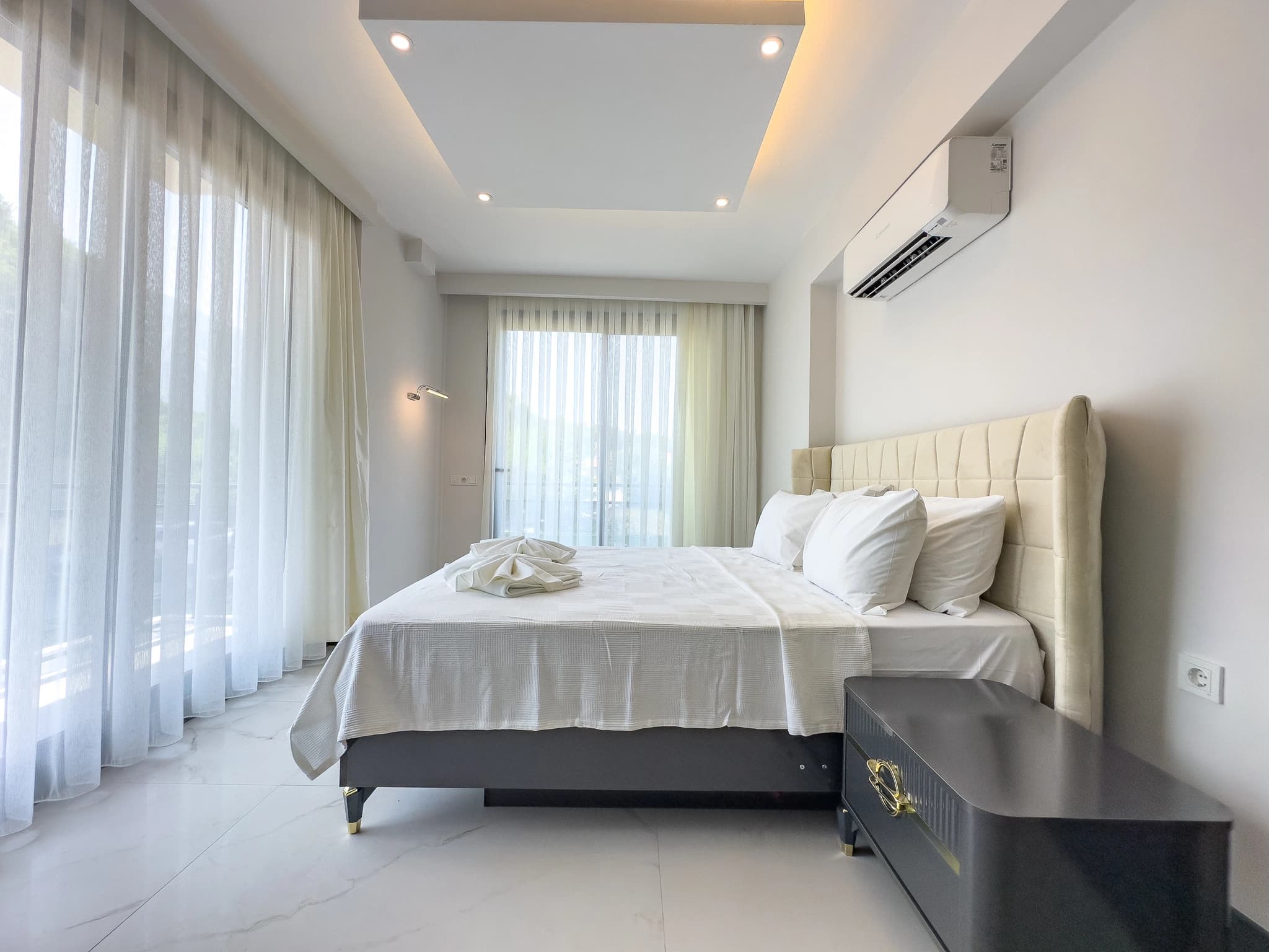 Elegant secondary bedroom with queen bed, cream upholstered headboard, and access to private balcony with landscape views.