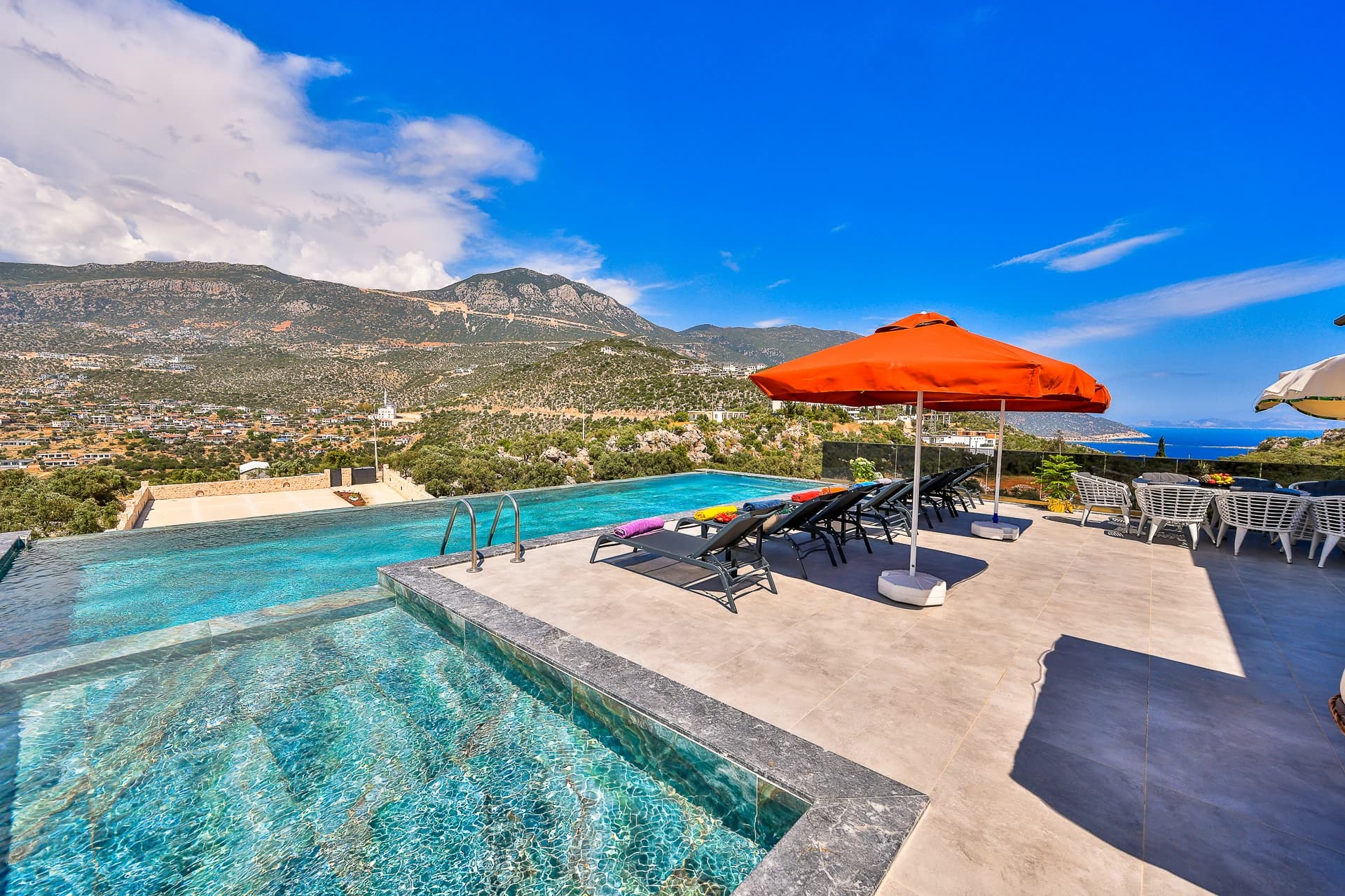Luxury pool area with sea views, lounge chairs, and orange parasol.