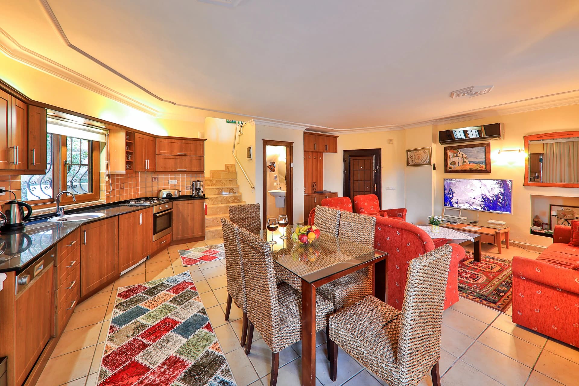 Dining area with wooden table and wicker chairs adjacent to kitchen and living space.