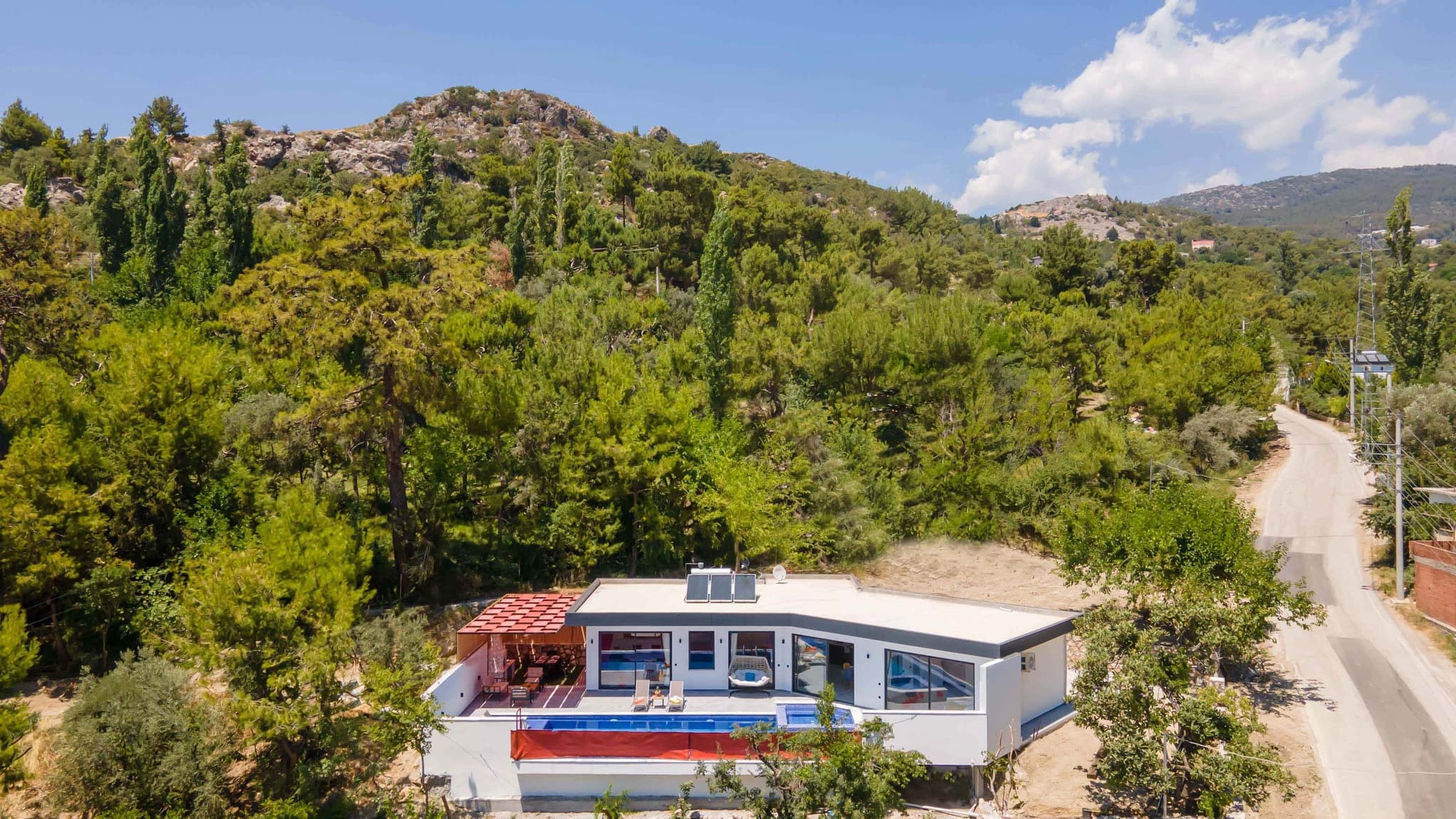 Secluded Garden Villa with Private Pool and Mountain Views in Kalkan – Contemporary villa exterior nestled in hillside forest setting with pool, red terrace canopy, and modern architecture.