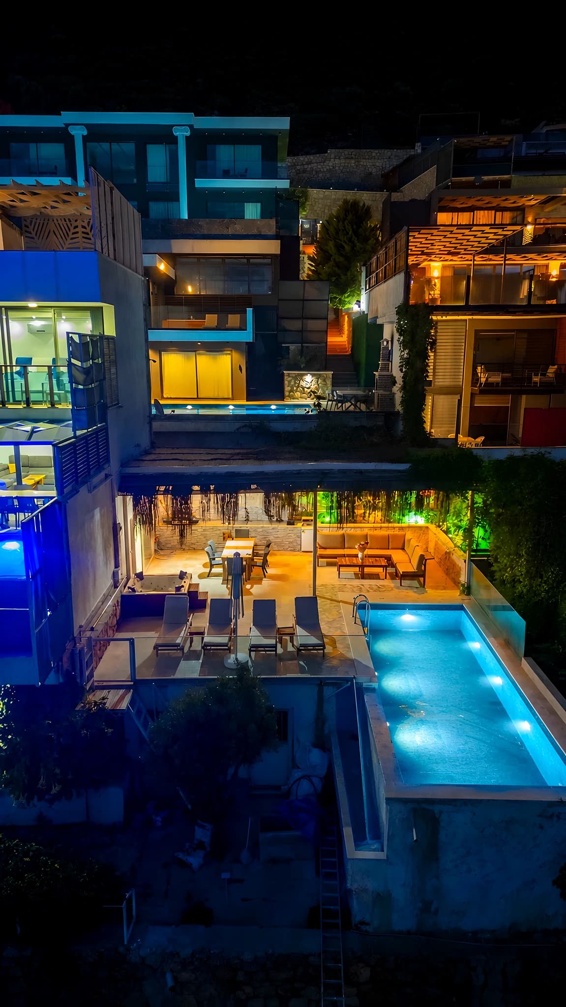 Nighttime aerial view of the villa's modern exterior with illuminated pool and lounge area.