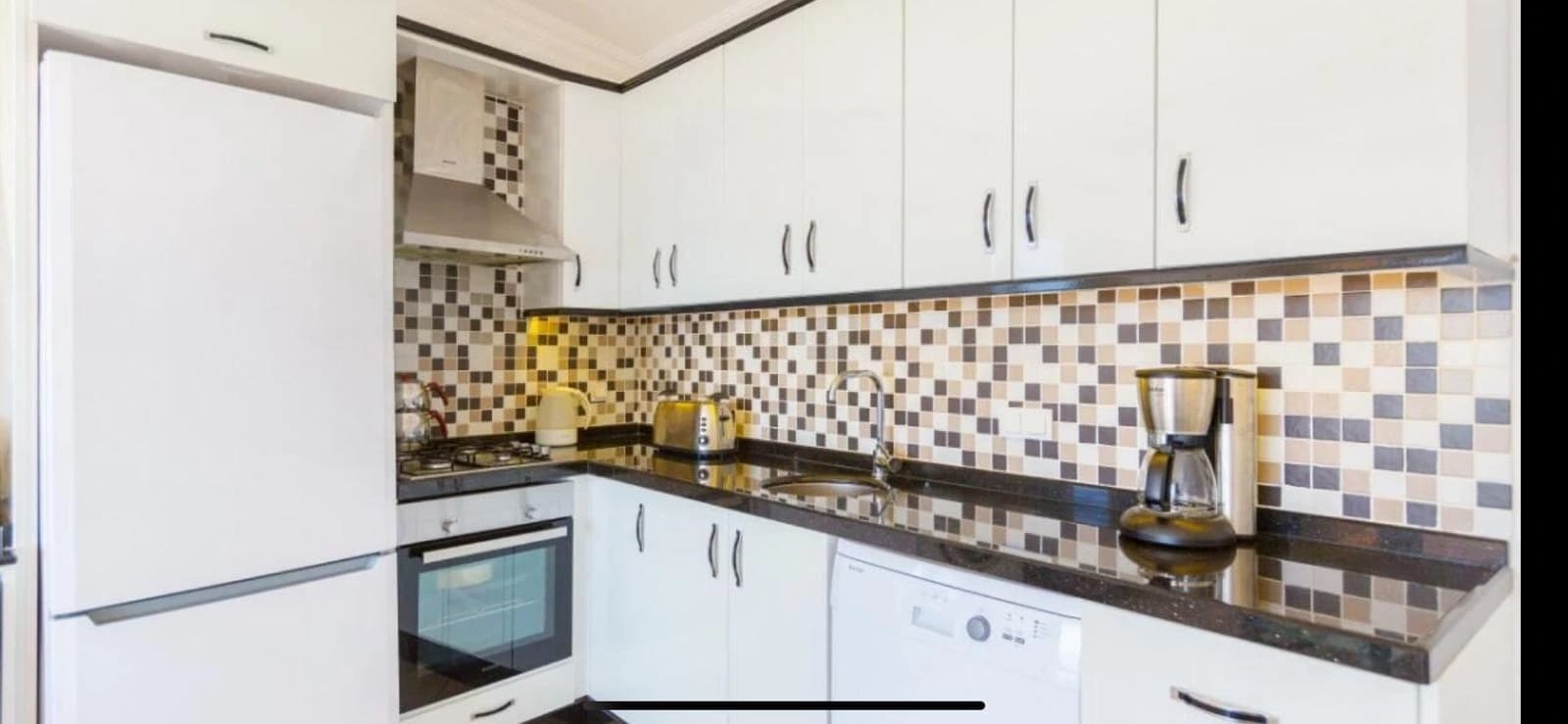 Compact kitchen with white cabinets and decorative mosaic tile backsplash.