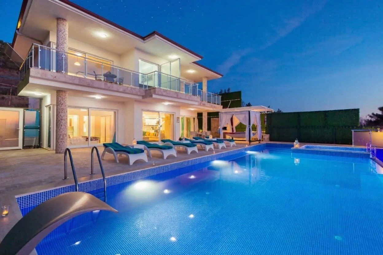 Stunning nighttime pool view with illuminated blue water and multiple sun loungers.