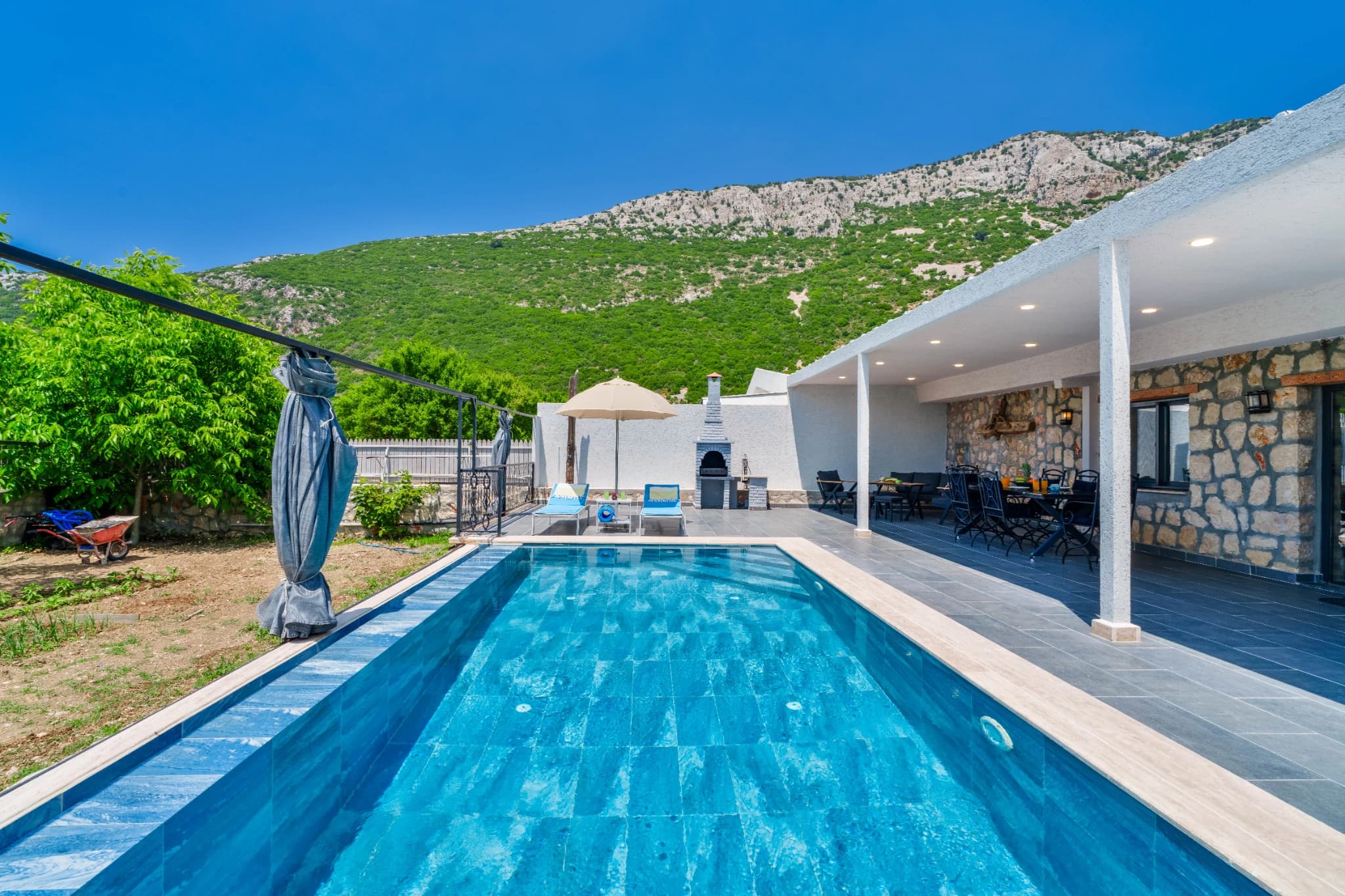 Pool with adjacent covered terrace and green hillside views.