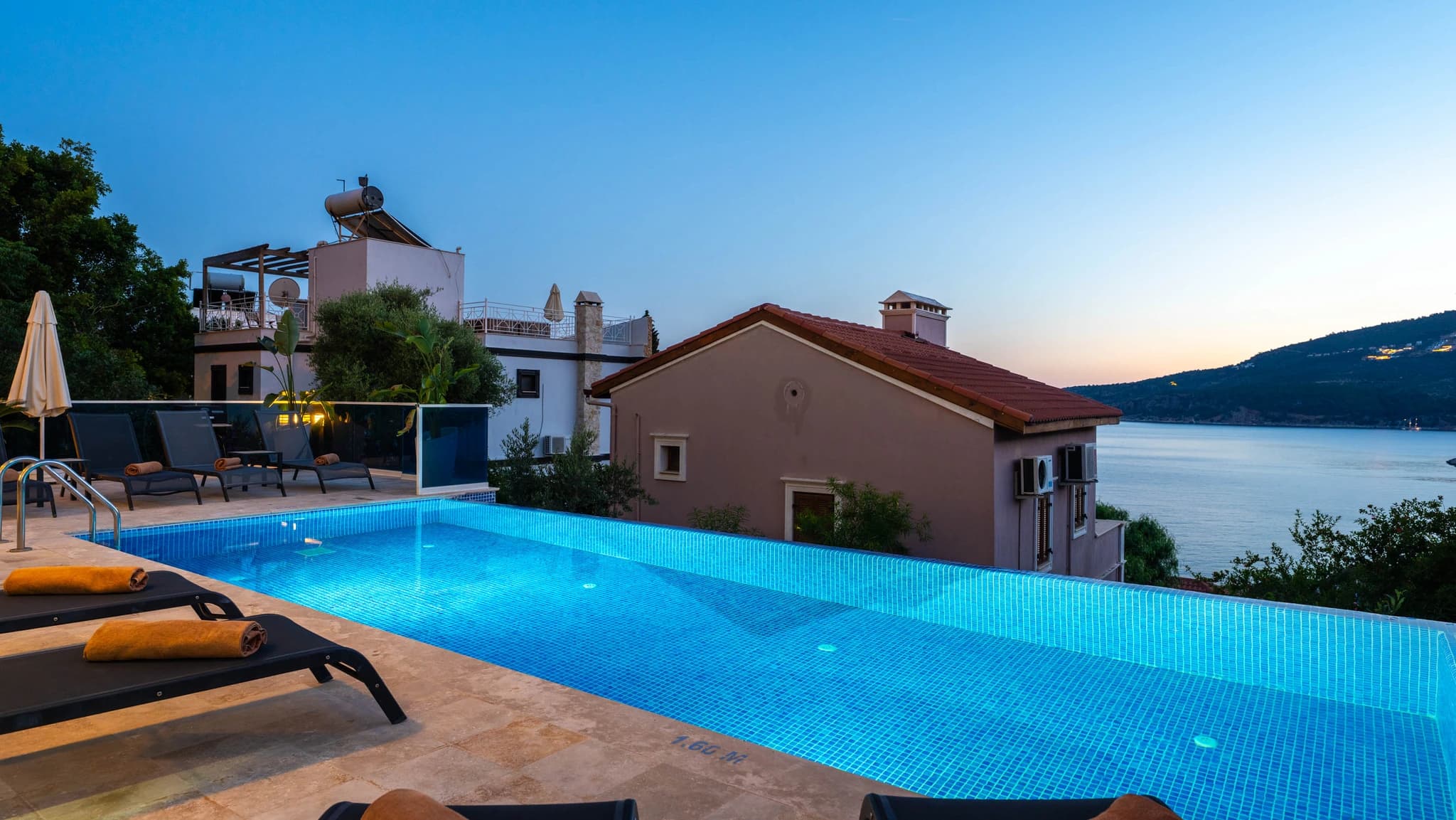 Expansive pool at dusk with loungers, parasol, and serene lake and mountain views.