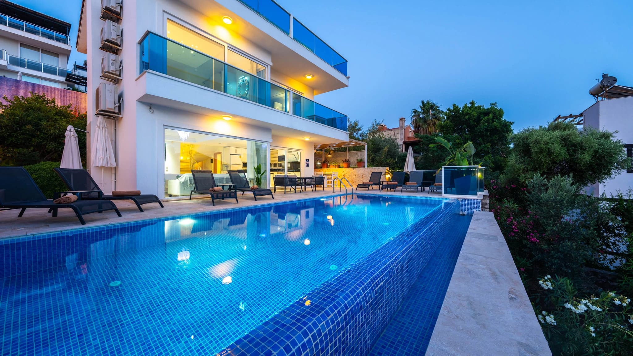 Evening-lit pool with loungers and modern villa architecture.