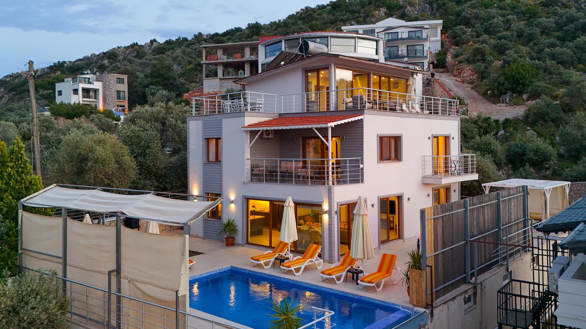 Stunning exterior view of the luxury villa with illuminated pool and multiple sun loungers at dusk.