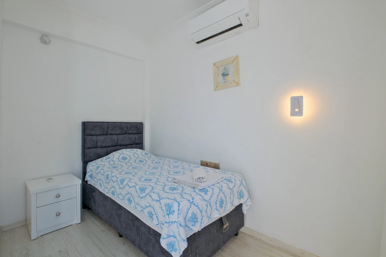 Simple, clean bedroom with a single bed, dark headboard, and essential furnishings.