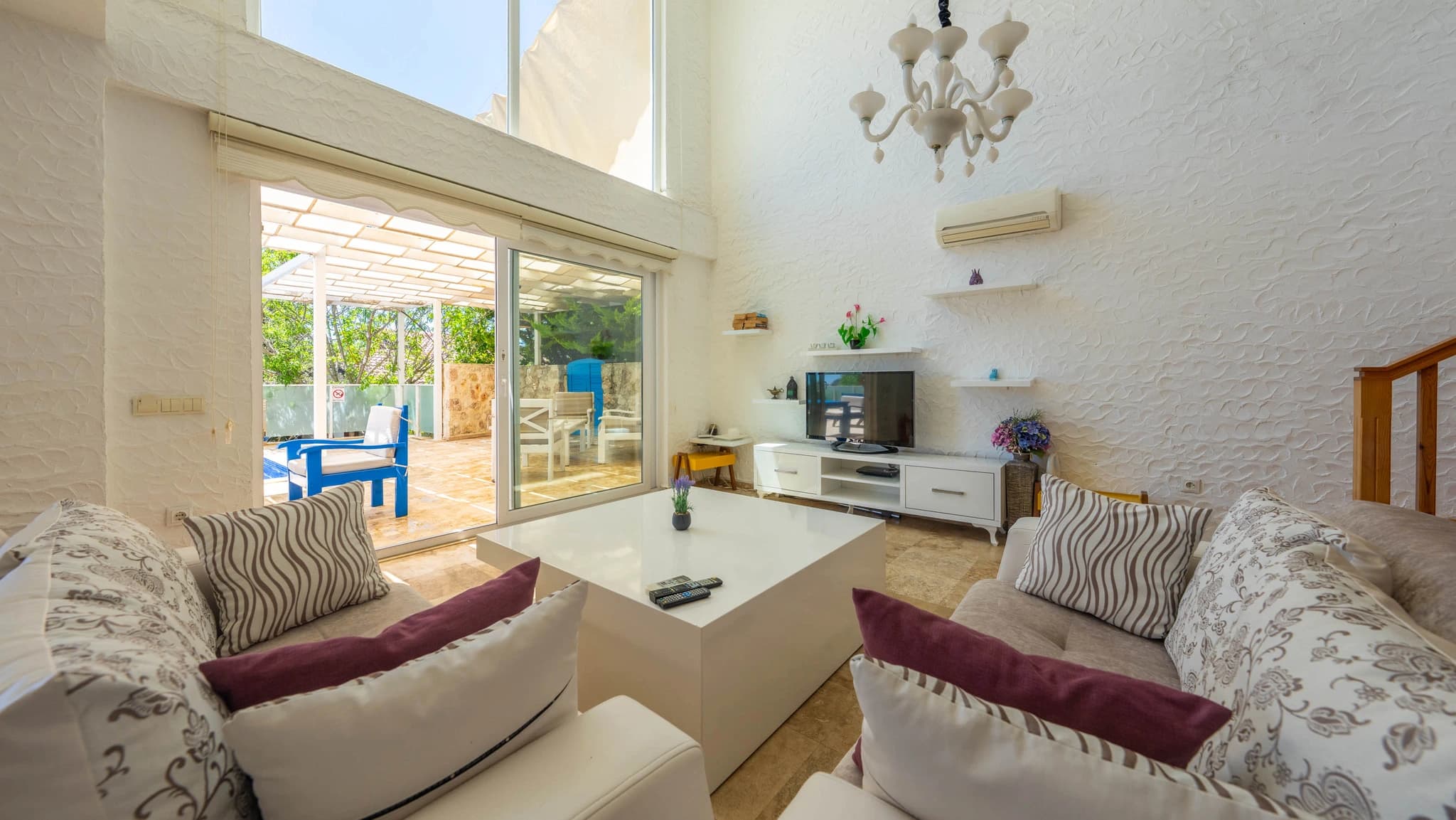 Light-filled living room with comfortable seating, TV, direct access to terrace and pool views.