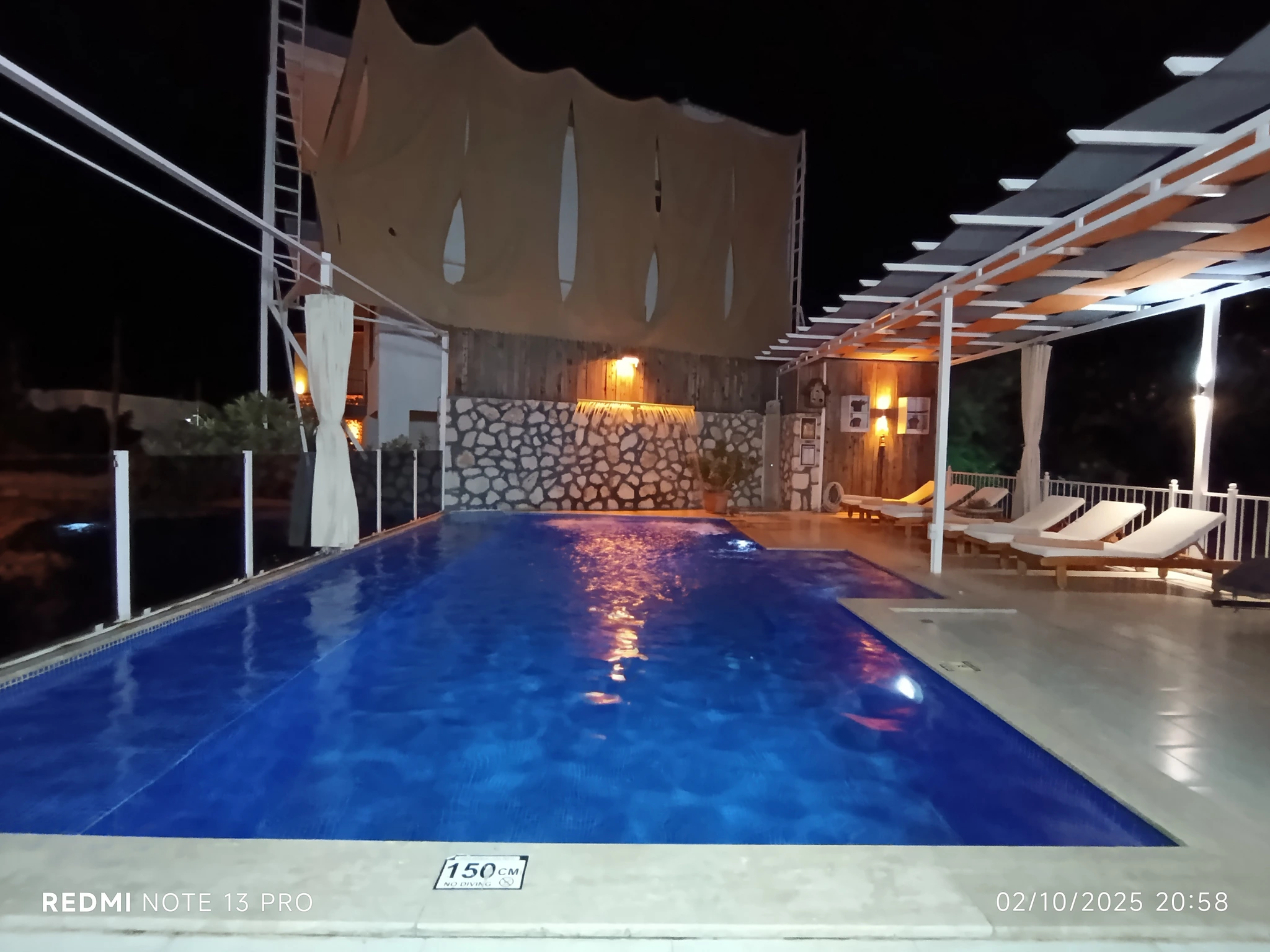 Geschützte Villa mit Naturblick, Privatpool und Garten in Kalkan – Stunning illuminated pool at night with white sun loungers and architectural pergola structure.