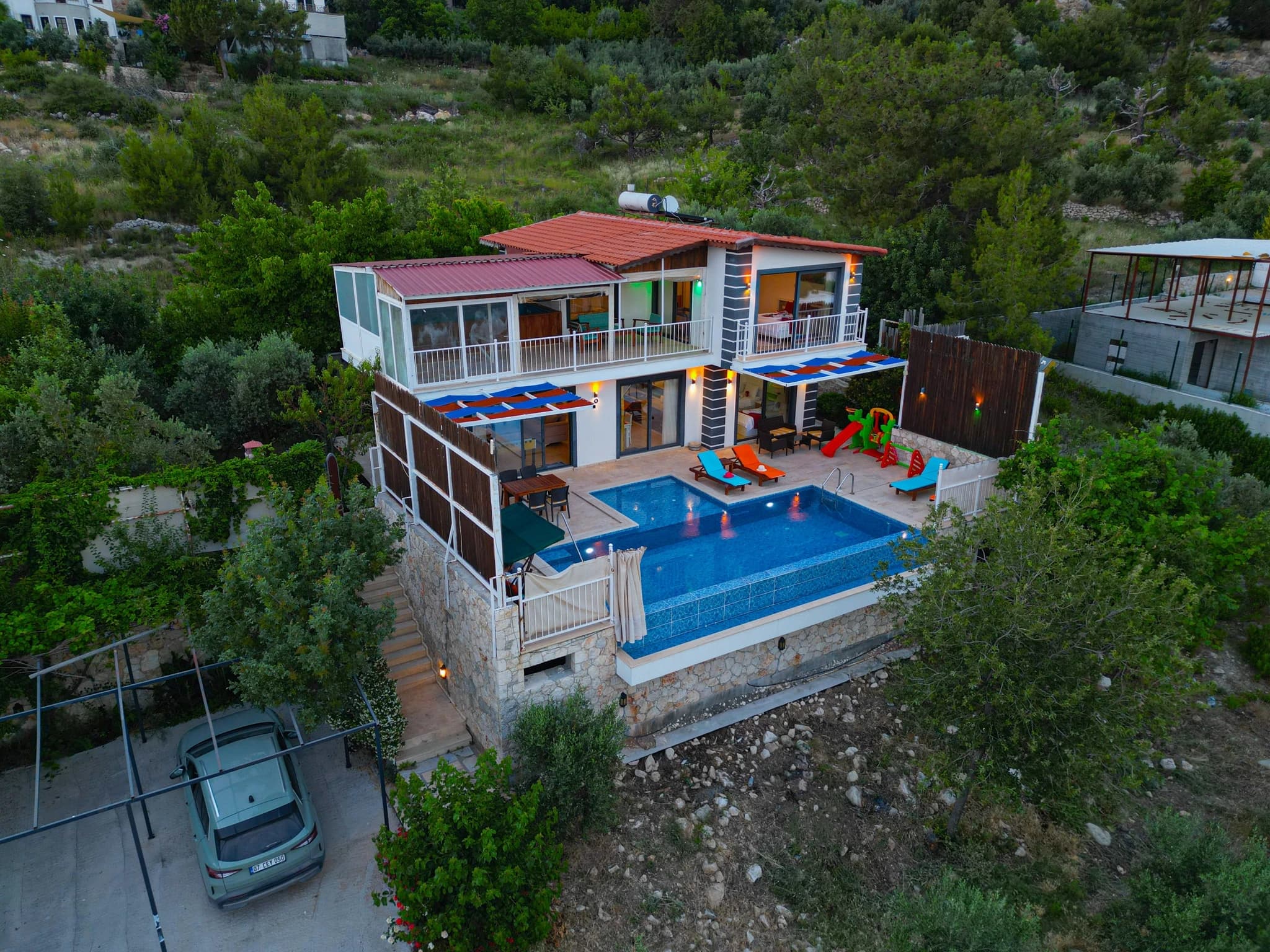 Abgeschiedene Villa mit Natur- und Bergblick, Innen- und Außenpool bei Kalkan – Evening exterior shot showcasing the villa's two-story design, pools, and hillside setting.