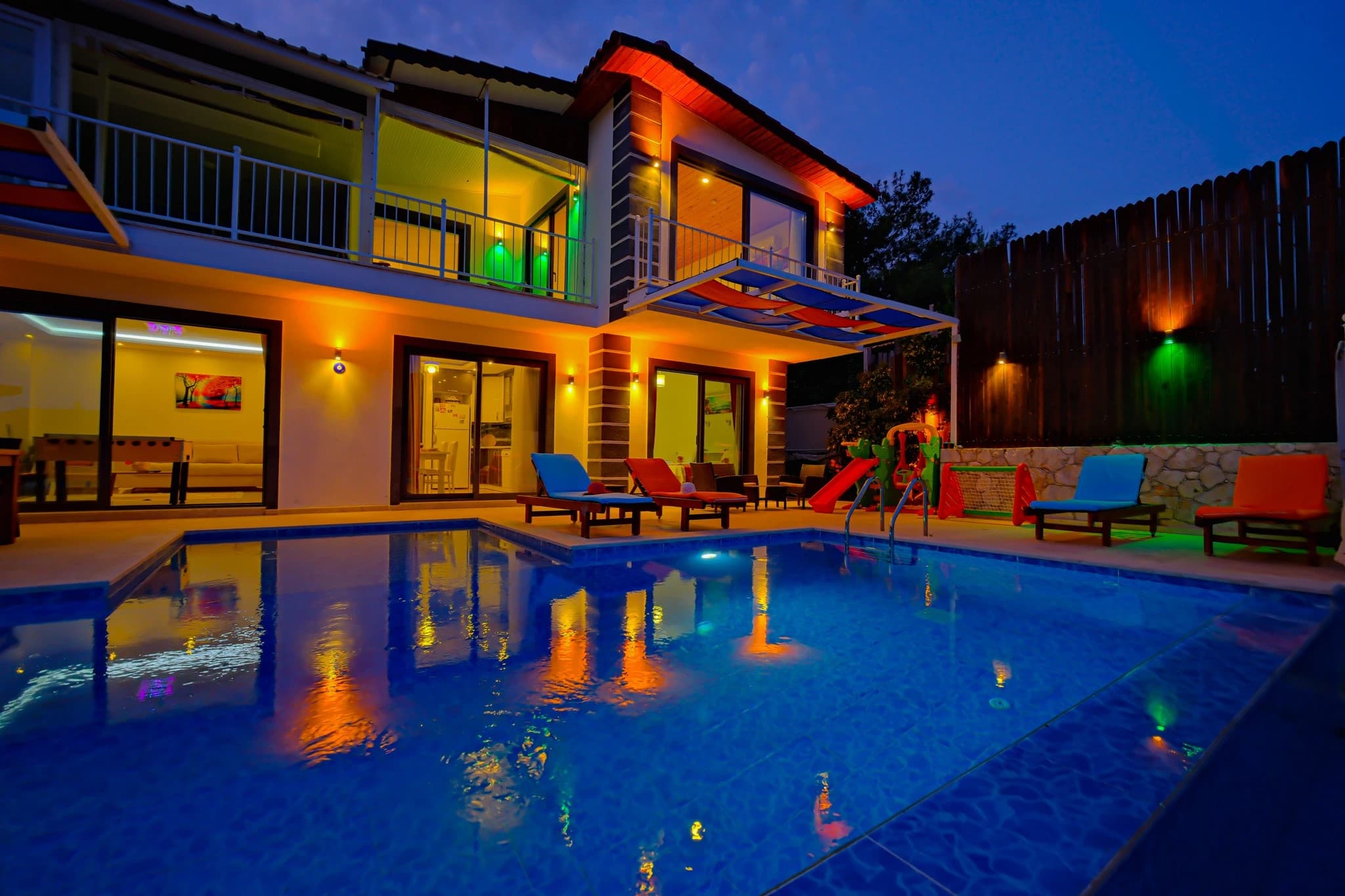 Abgeschiedene Villa mit Natur- und Bergblick, Innen- und Außenpool bei Kalkan – Night view of the contemporary villa exterior featuring the glowing pool, colorful loungers, illuminated two-level façade, and upper terrace.