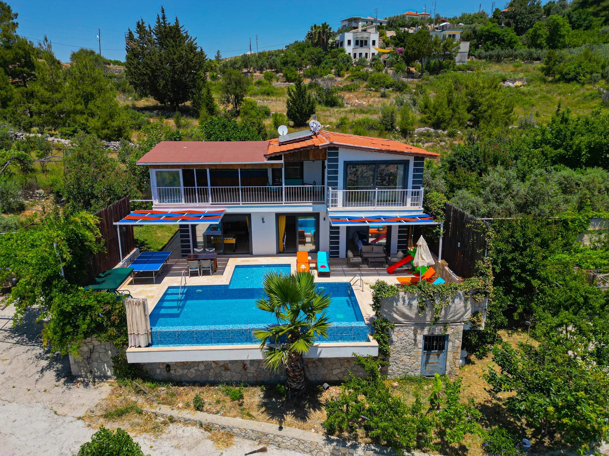 Abgeschiedene Flitterwochen-Villa mit privatem und beheiztem Pool bei Kalkan – Aerial view of the modern villa exterior with illuminated blue pool, colorful loungers, and covered terrace areas.