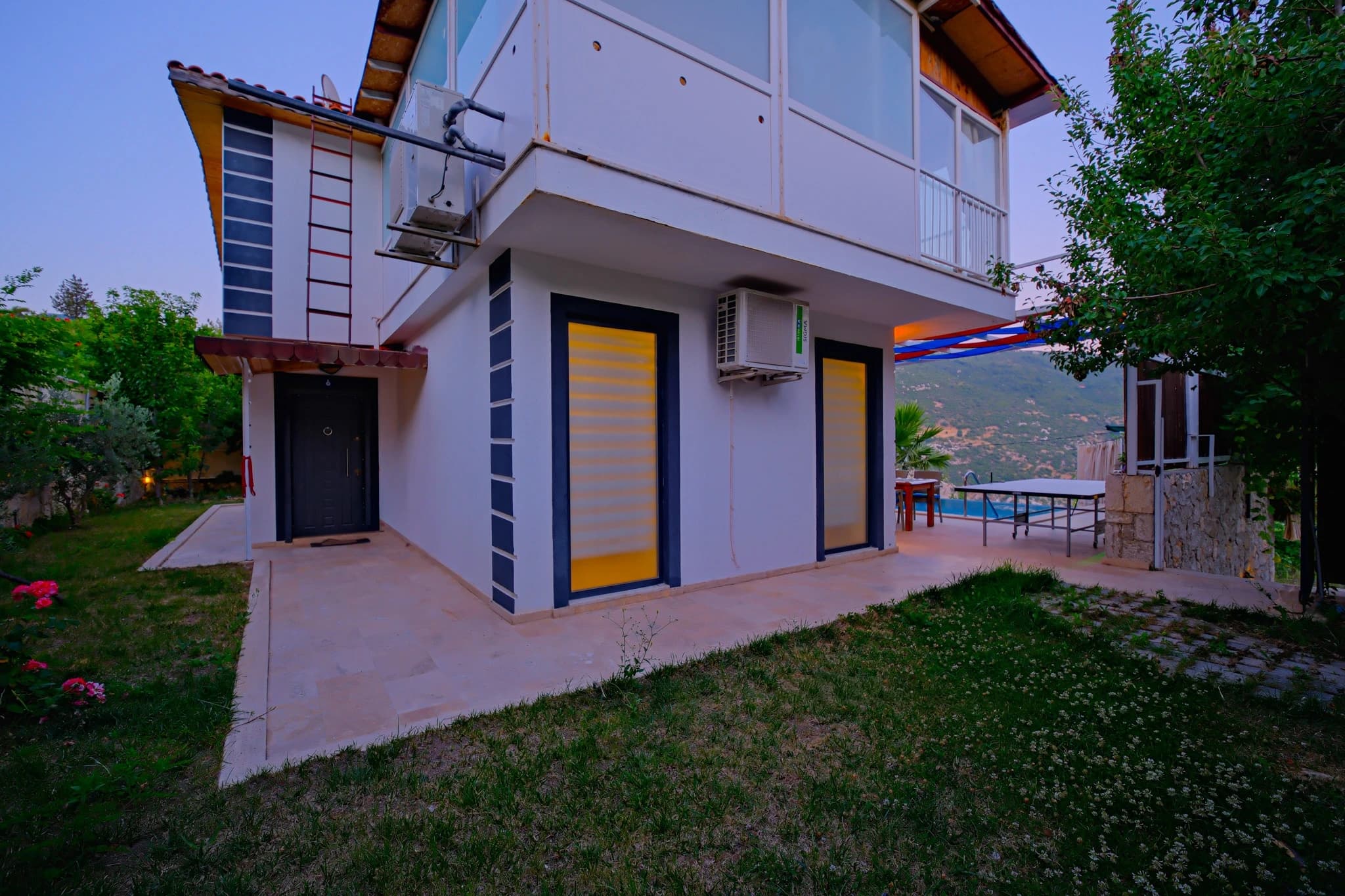 Abgeschiedene Flitterwochen-Villa mit privatem und beheiztem Pool bei Kalkan – Modern villa exterior with bright yellow doors, upper-level balcony, and distant mountain views.