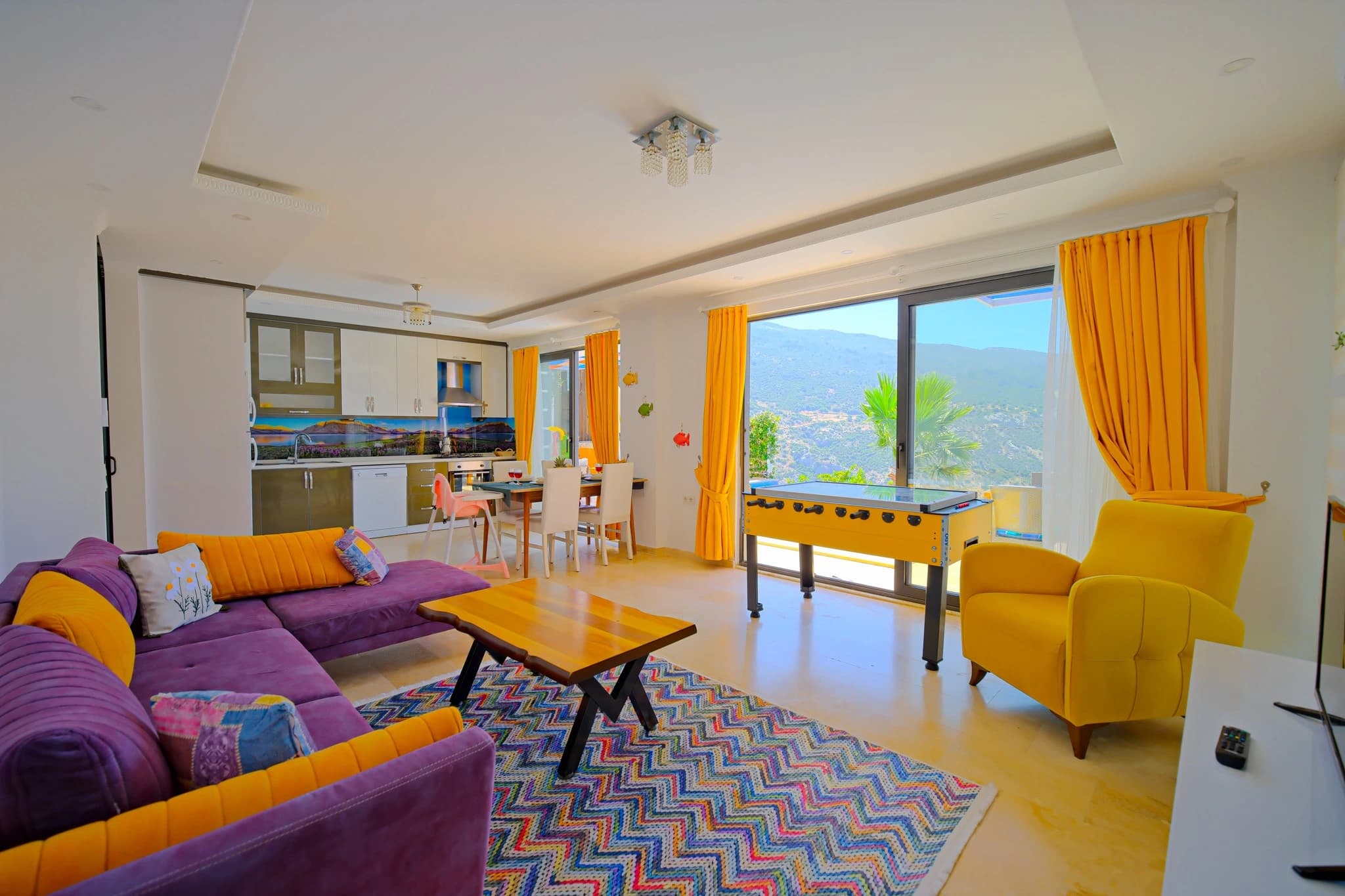 Abgeschiedene Flitterwochen-Villa mit privatem und beheiztem Pool bei Kalkan – Spacious living area with vibrant purple seating, foosball table, and panoramic mountain views through large windows.