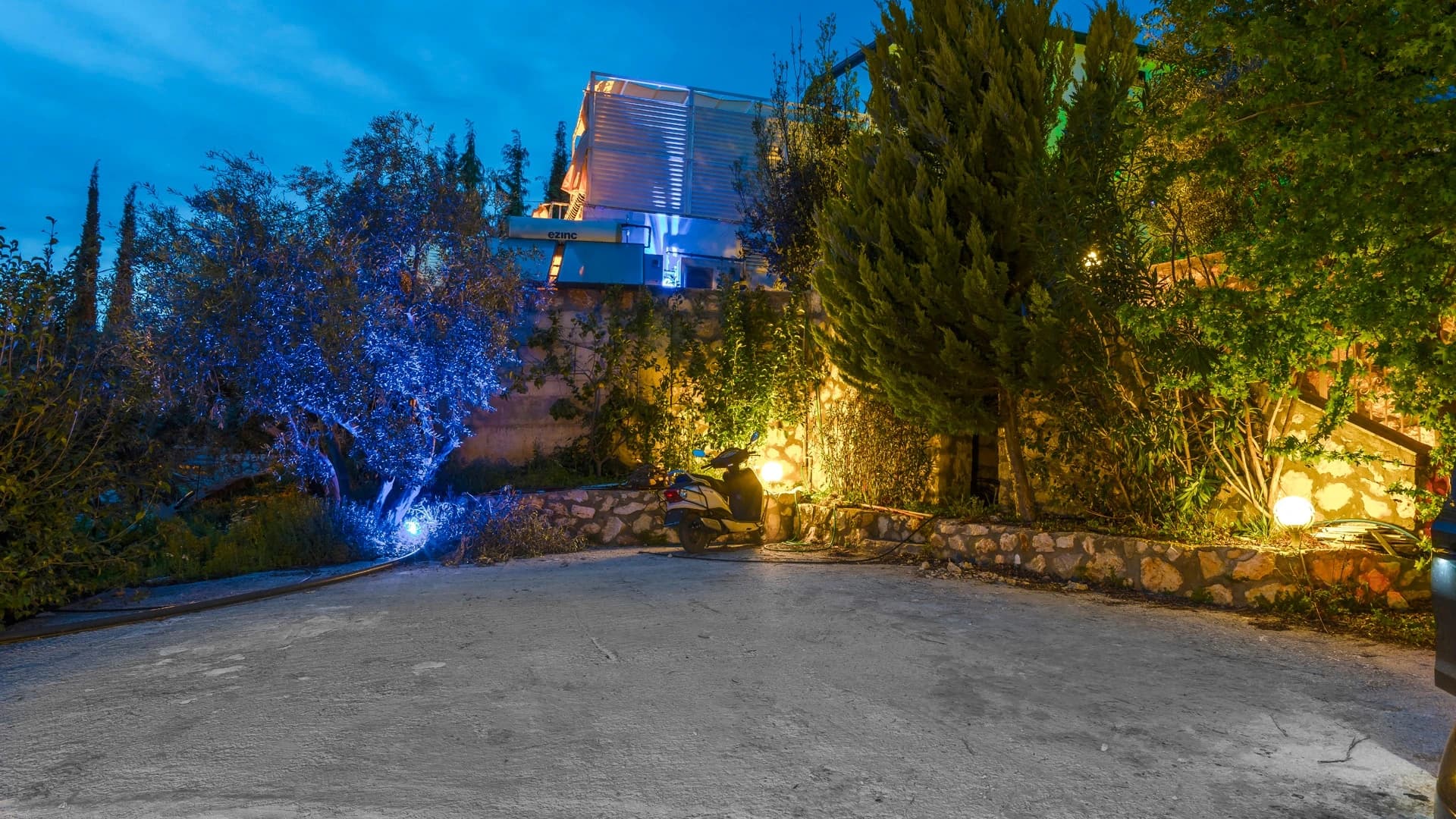 Secluded Nature Retreat Villa with Heated Pool and Sea & Mountain Views in Kalkan – Elegant villa entrance with dramatic nighttime illumination, cypress landscaping, and stone architecture.