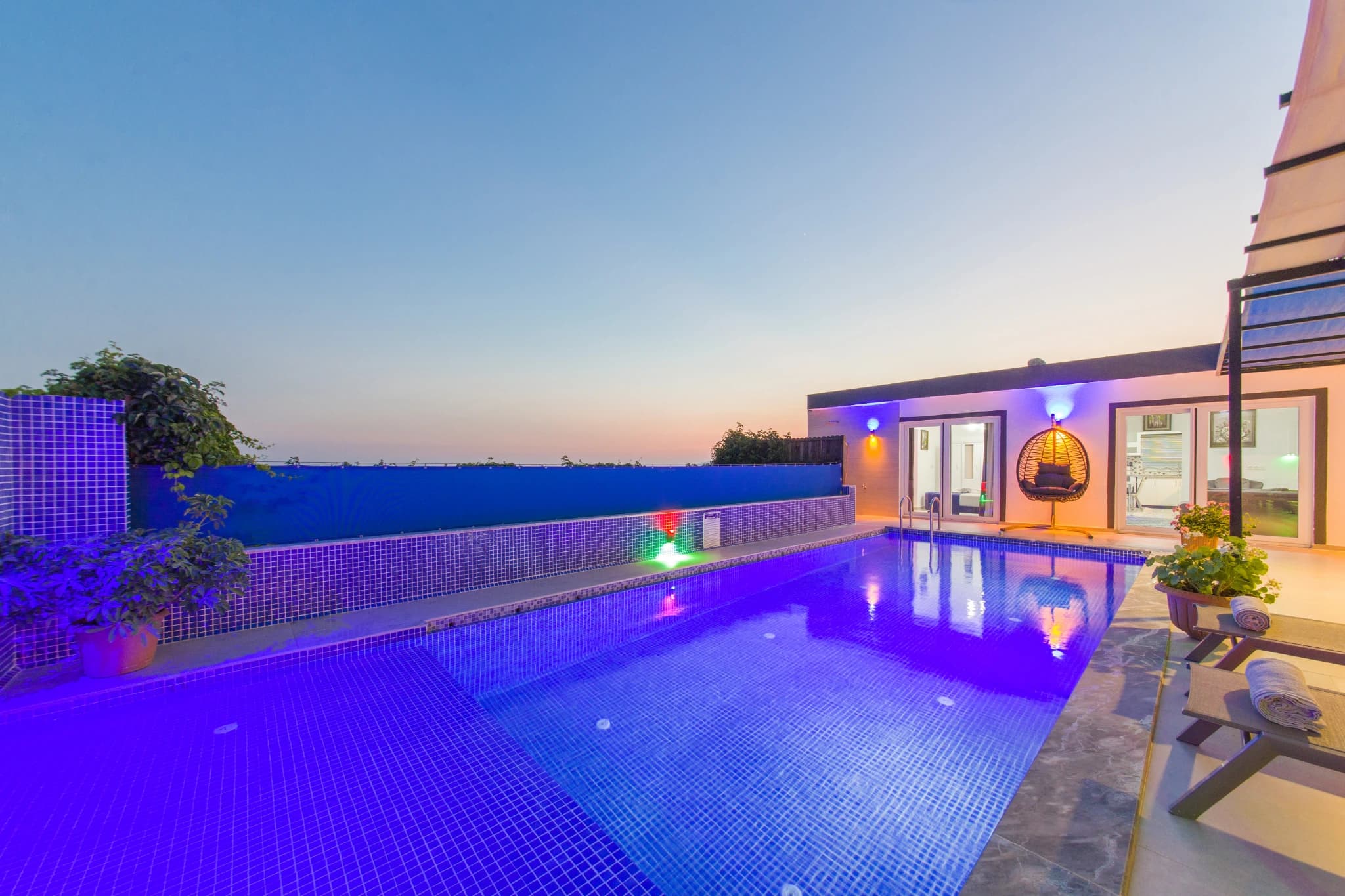 Stunning twilight view of the lit private pool with modern lounge chairs and mountain backdrop.