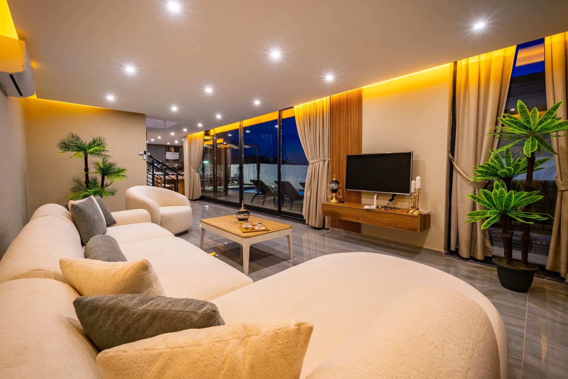 Elegant living area with curved seating, entertainment setup, and evening illuminated balcony access.