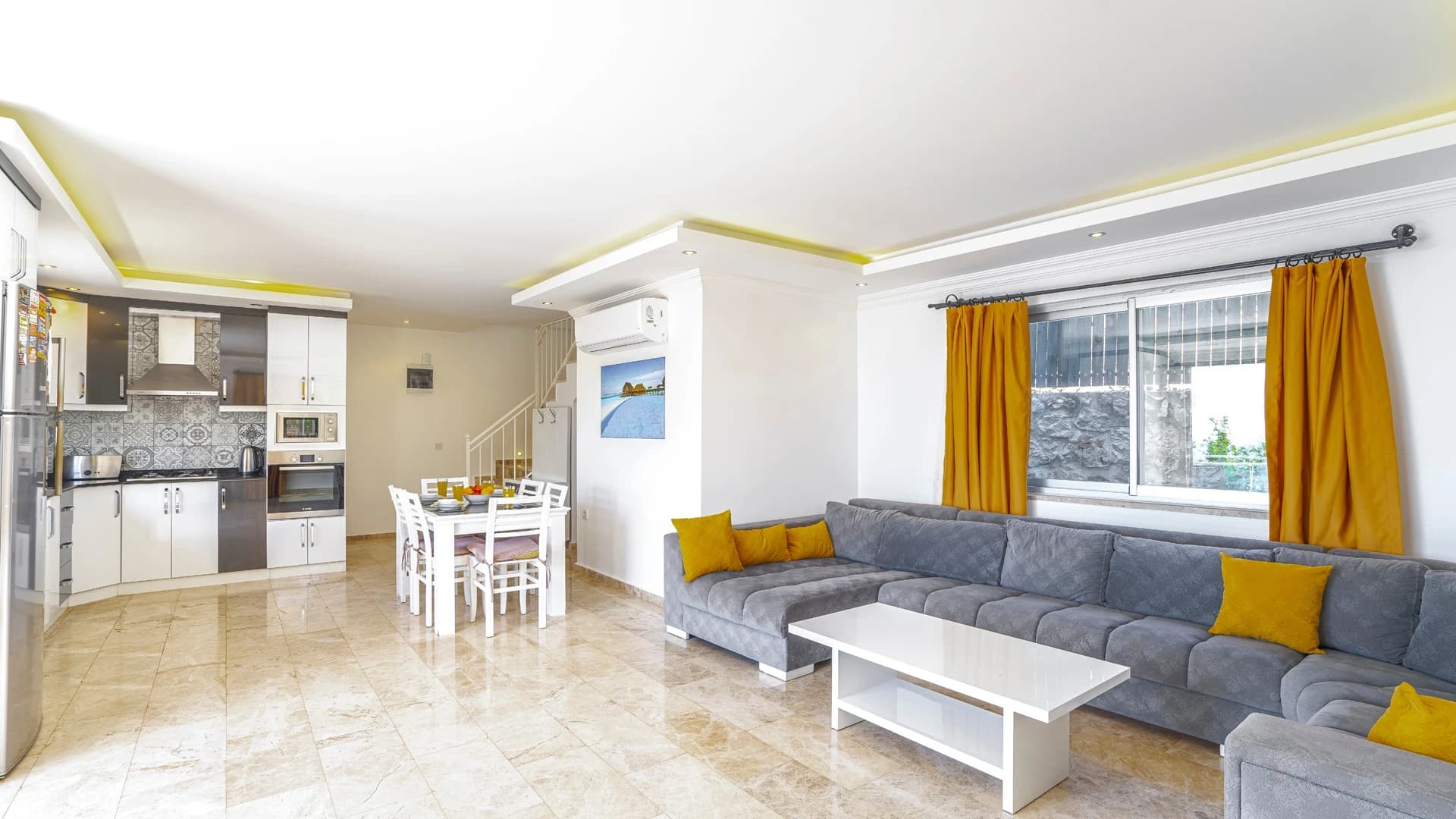 Secluded 2-Bedroom Villa with Heated Pool and Mountain & Sea Views in Kalkan – Contemporary living room with gray sectional sofa, yellow accessories, and integrated kitchen.