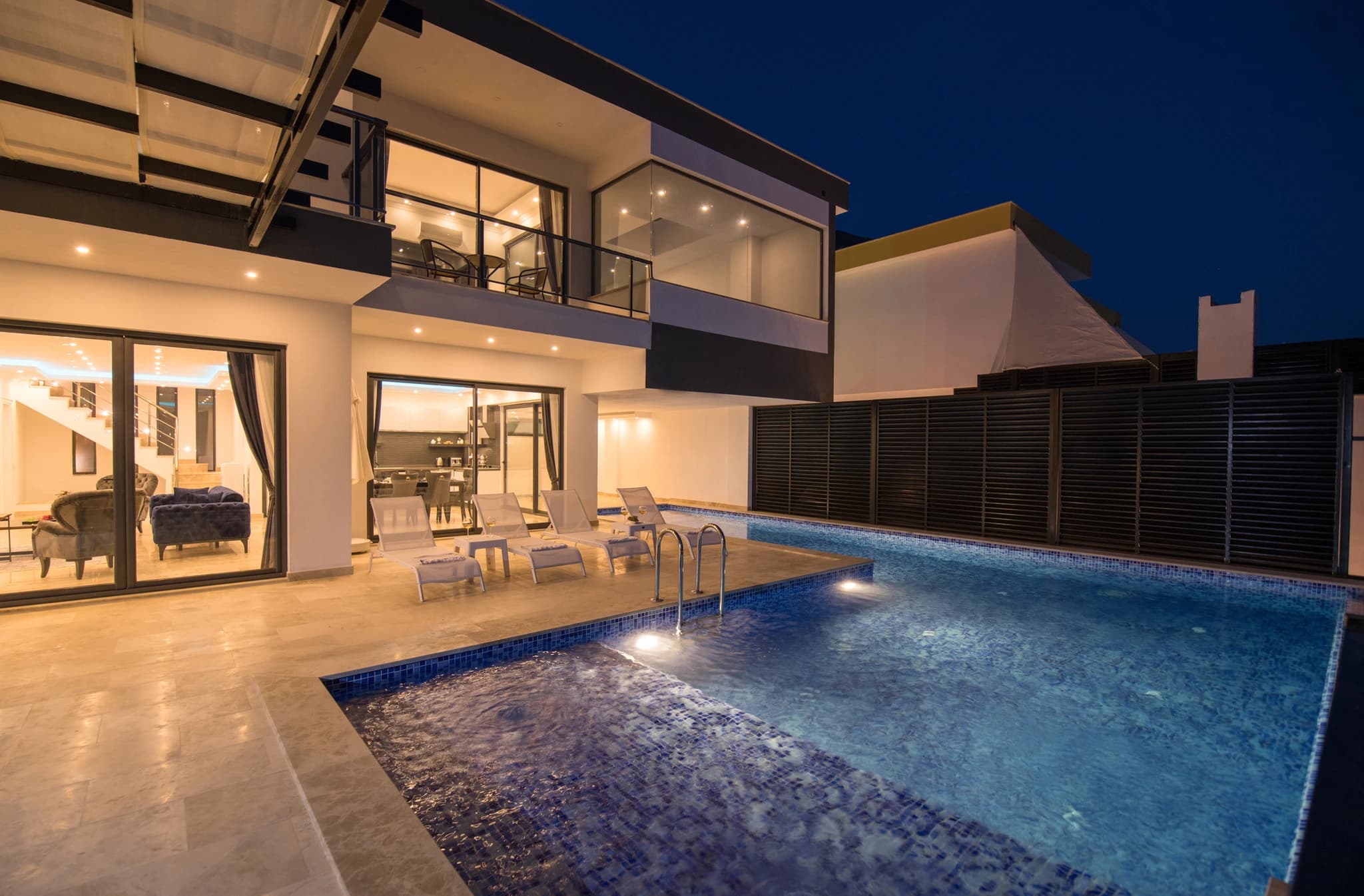 Secluded Honeymoon Villa with Private & Heated Indoor Pool in Kalkan – Stunning nighttime pool area with illuminated water, sun loungers, and modern villa interior visible through glass doors.
