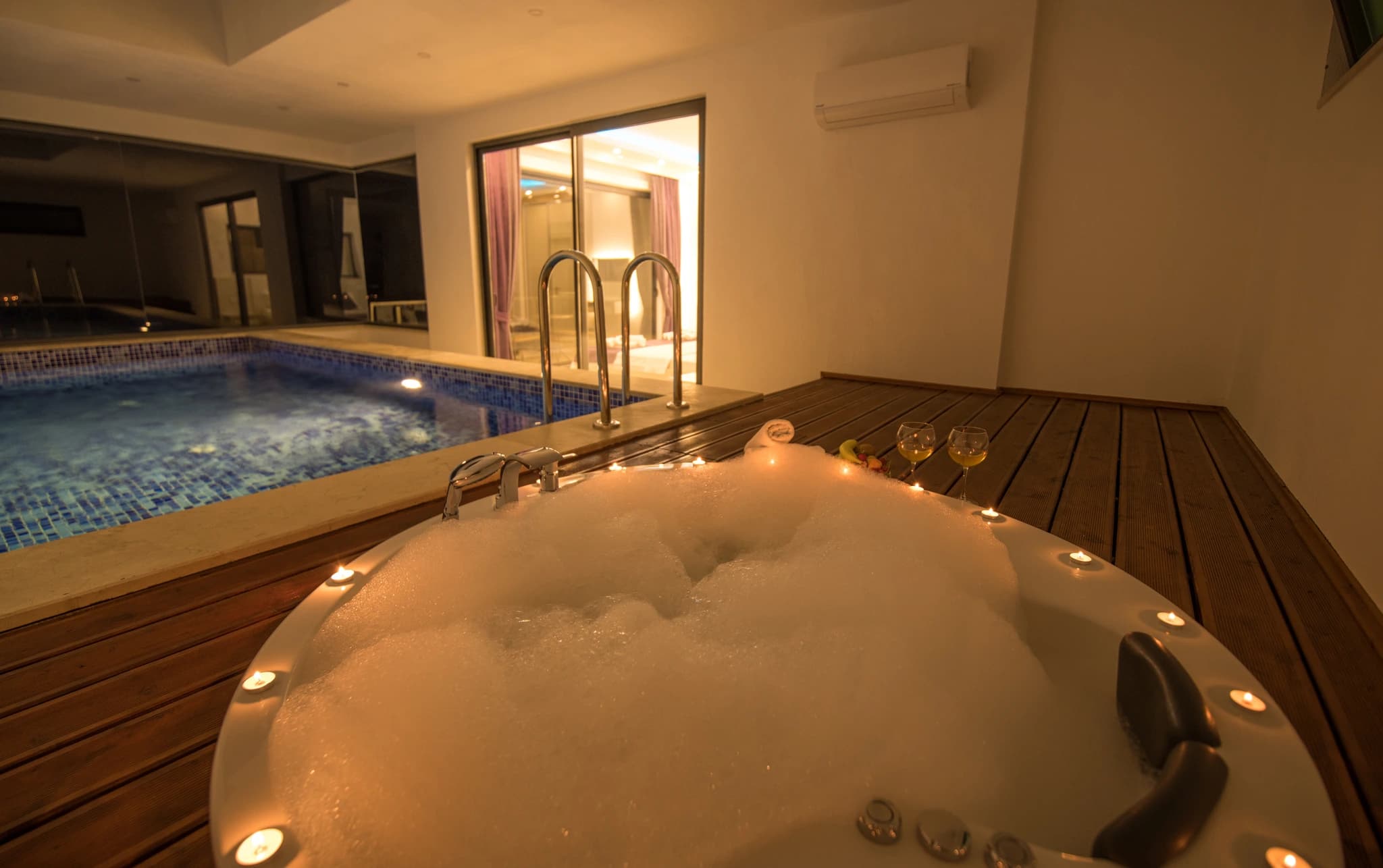 Secluded Honeymoon Villa with Private & Heated Indoor Pool in Kalkan – Luxurious indoor spa with hot tub in foreground and swimming pool, beautifully lit for evening relaxation.
