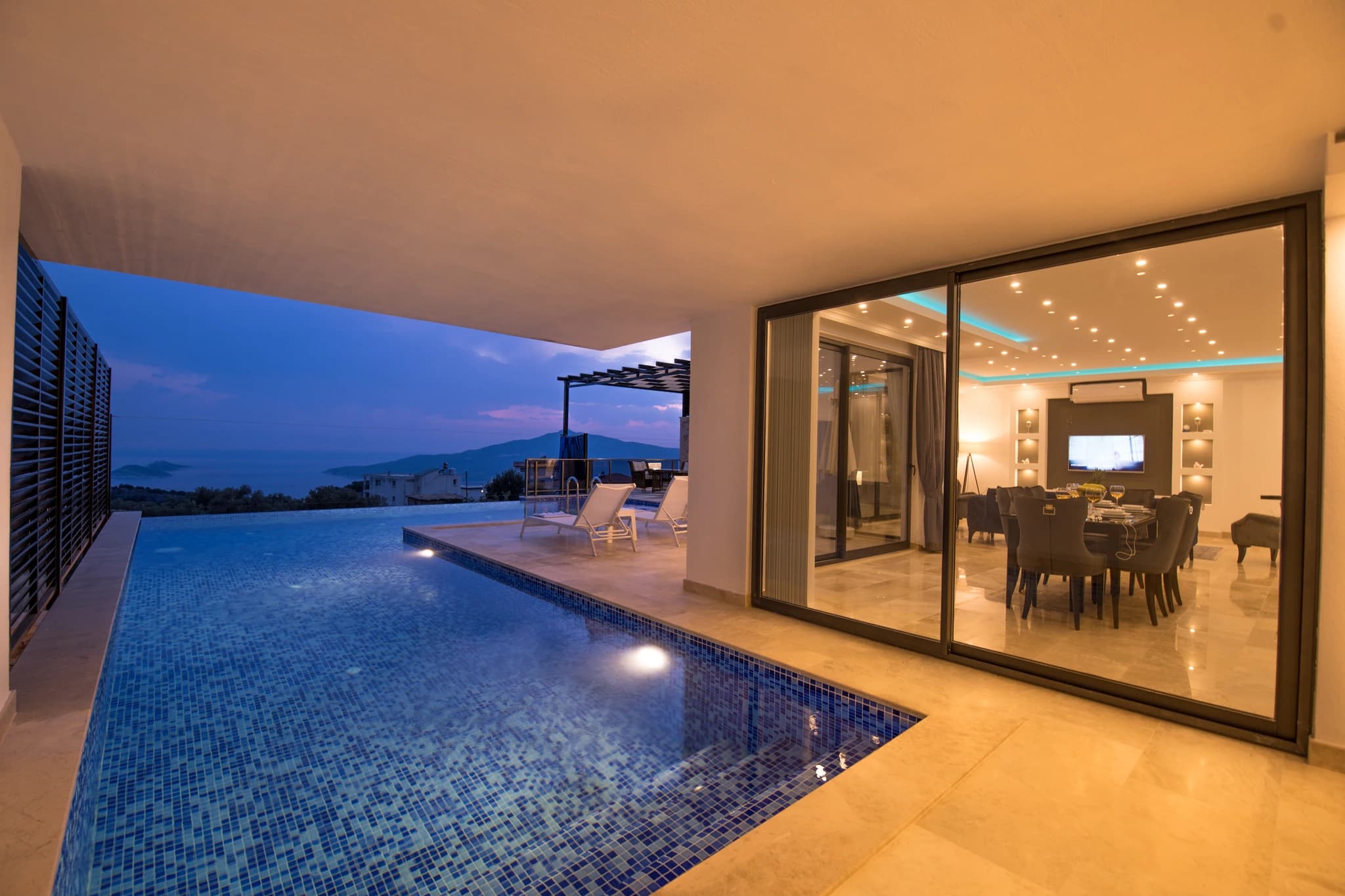 Secluded Honeymoon Villa with Private & Heated Indoor Pool in Kalkan – Stunning illuminated pool overlooking mountains, with adjacent terrace and lounge chairs.