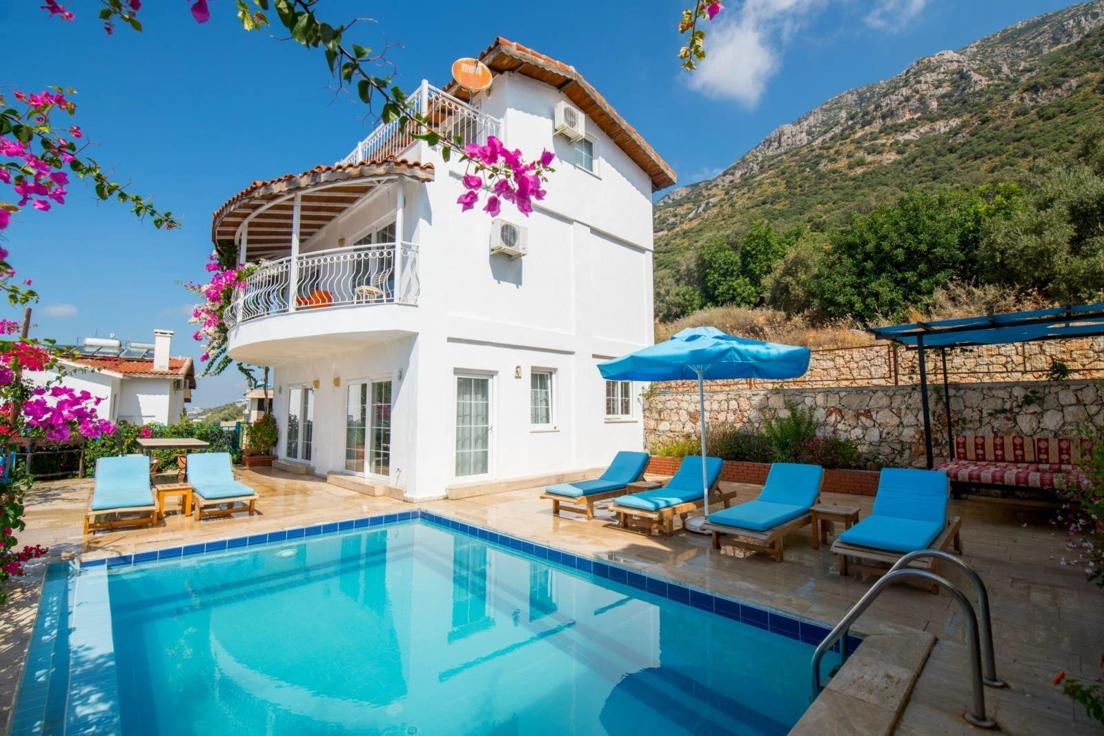 Private villa pool with blue loungers, magenta flowers, and mountain views.